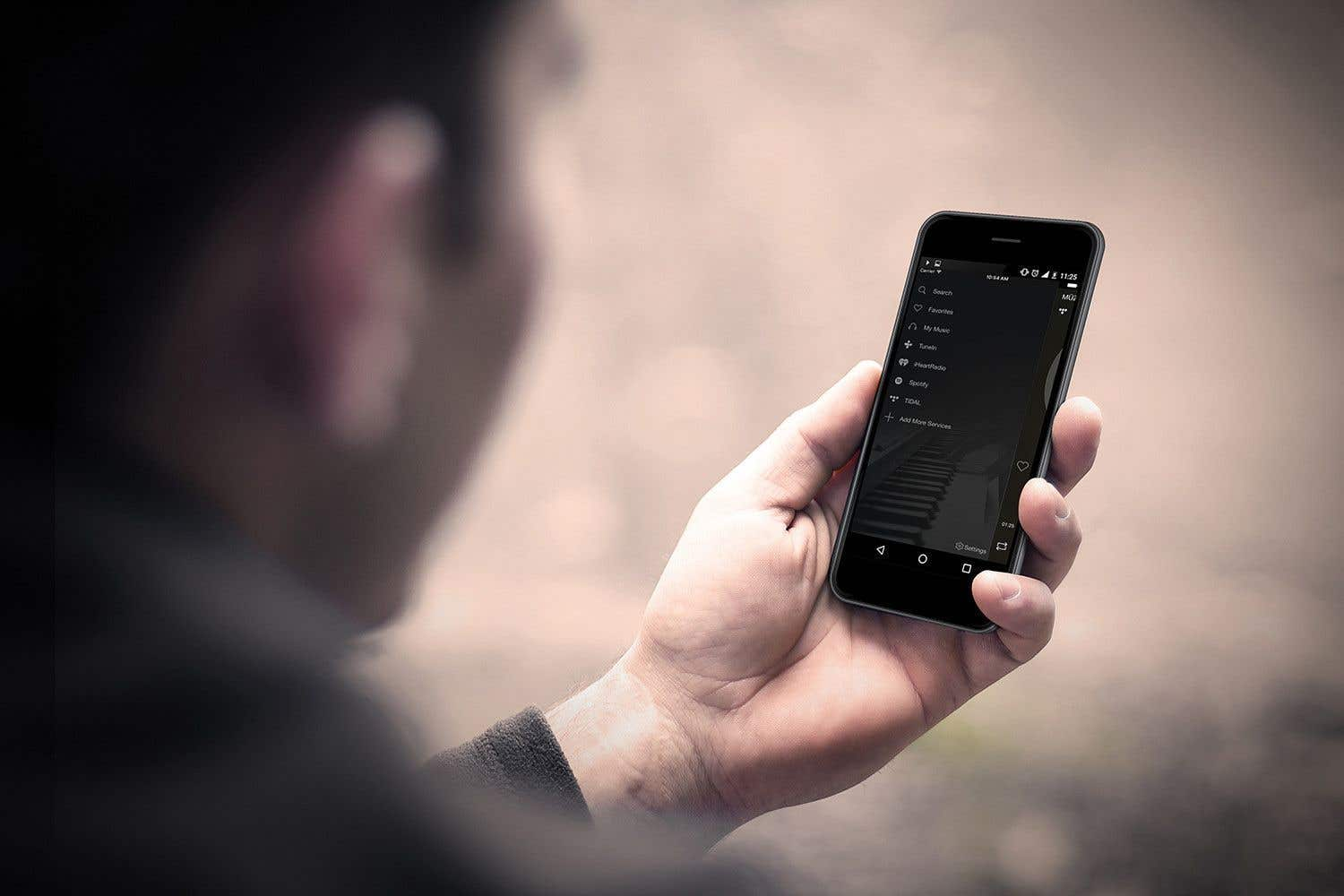 Una persona sostiene un teléfono inteligente que muestra una aplicación de música con varios servicios.