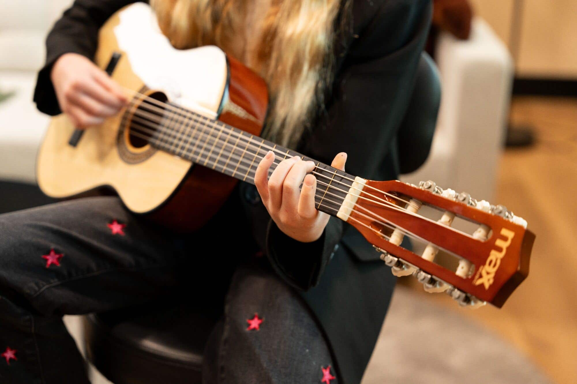 Persoon speelt akoestische gitaar met sterrenpatroon op broek.