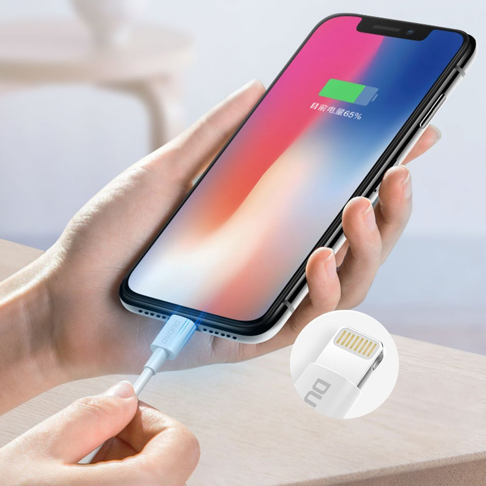 Una mano inserisce un cavo di ricarica bianco in uno smartphone che mostra il 65% di carica.