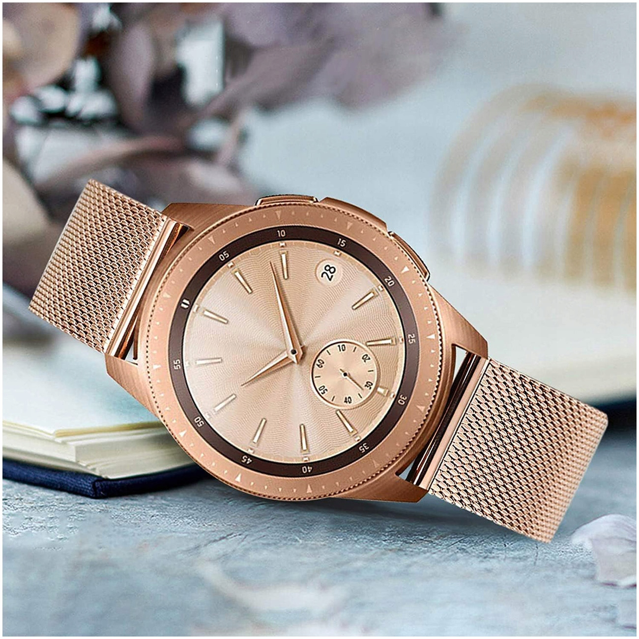 Różowo-złoty smartwatch z siateczkową bransoletą spoczywa na książkach.