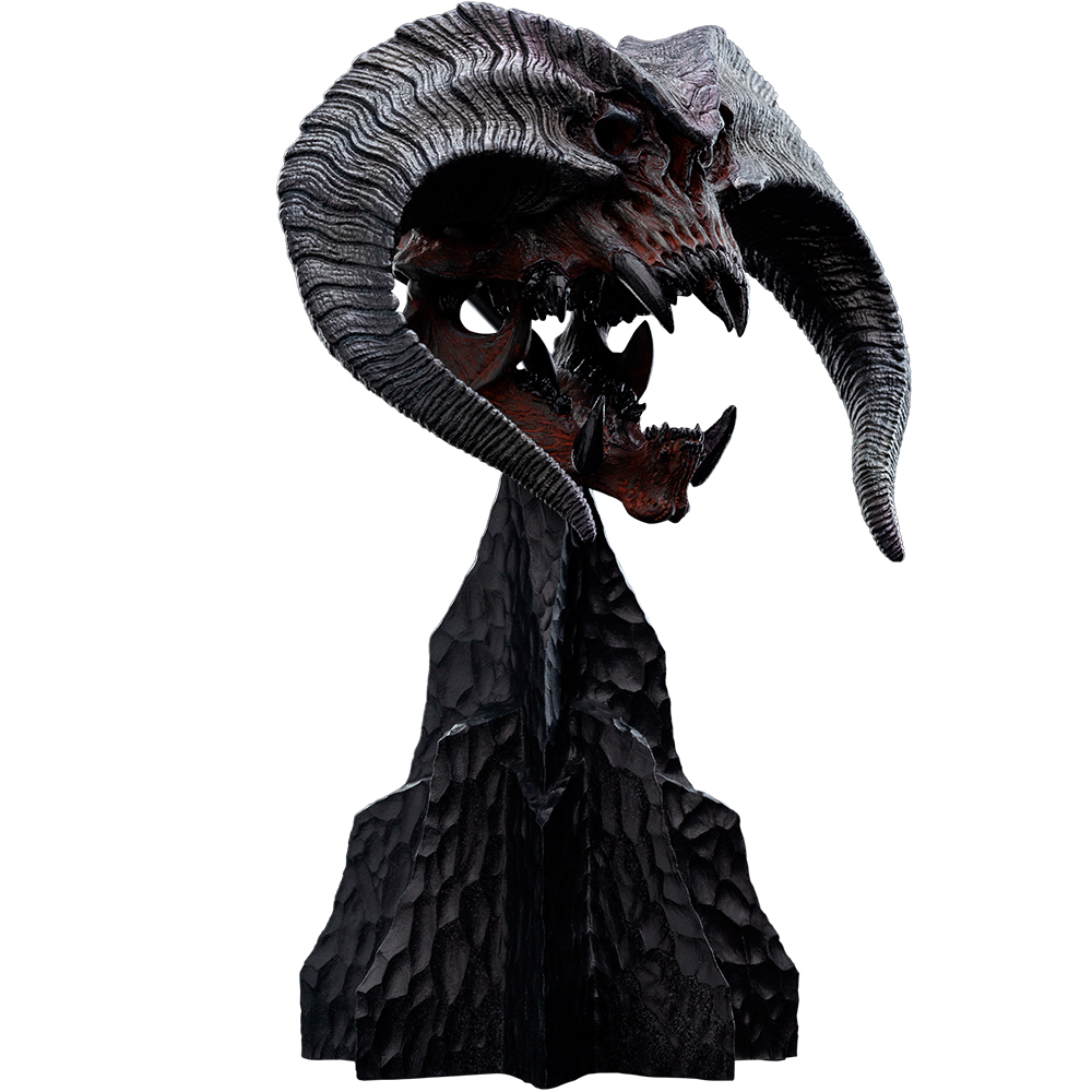 Una escultura oscura de un cráneo demoníaco con cuernos, sobre una base rocosa.