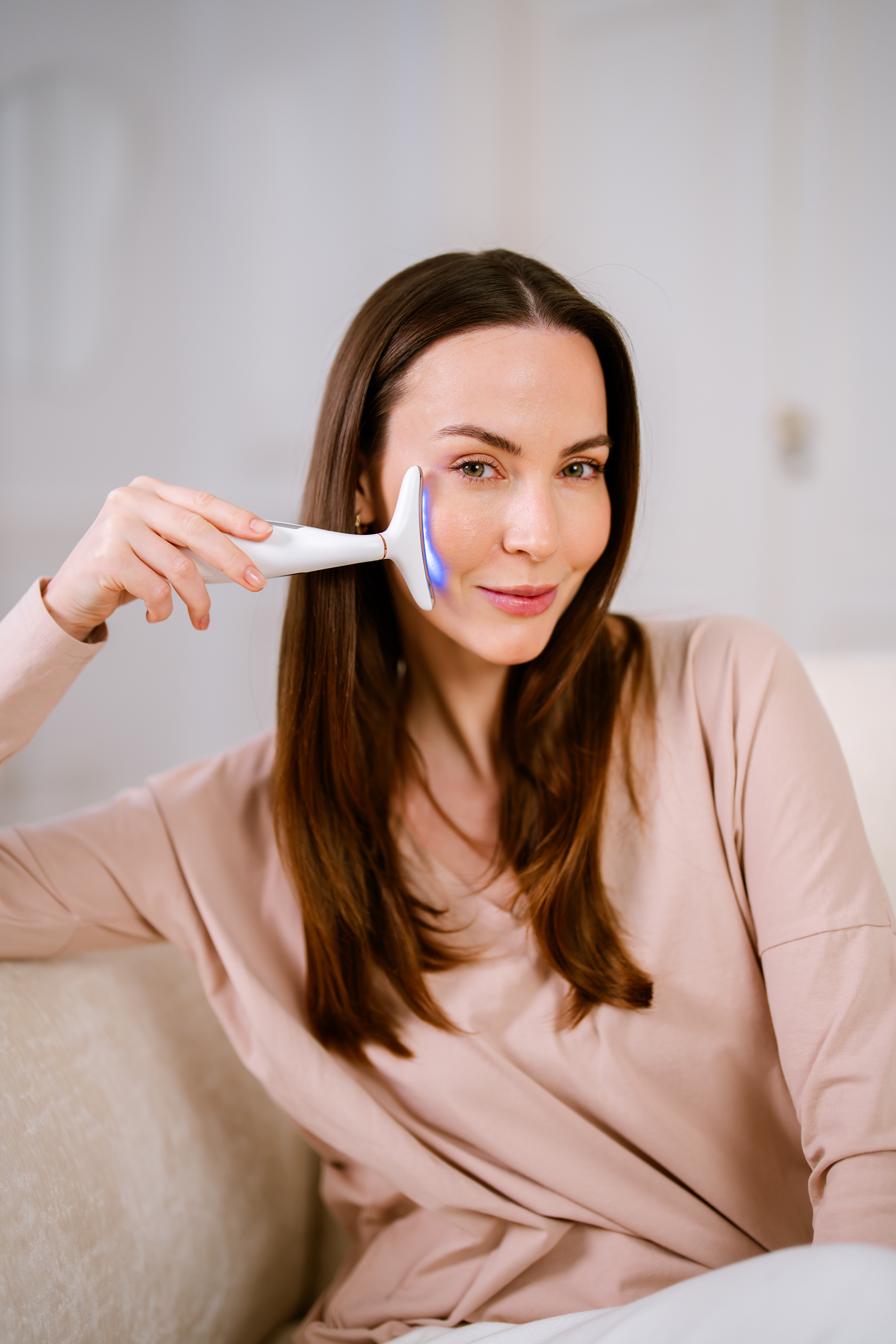 Una mujer usa un dispositivo de cuidado de la piel con luces azules en su rostro.