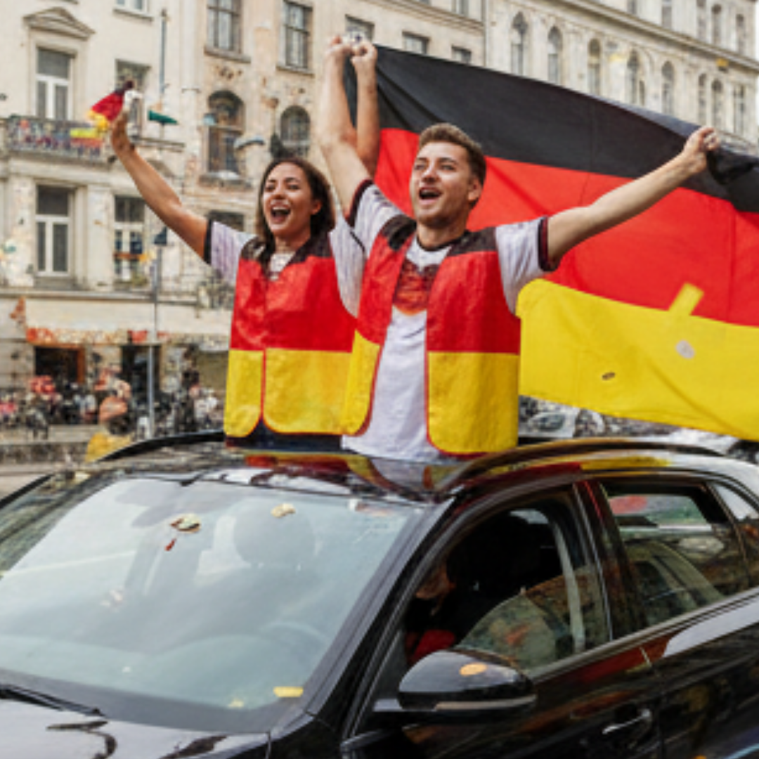 Zwei Fans in Deutschland-Westen stehen auf einem Auto mit Deutschlandflagge.