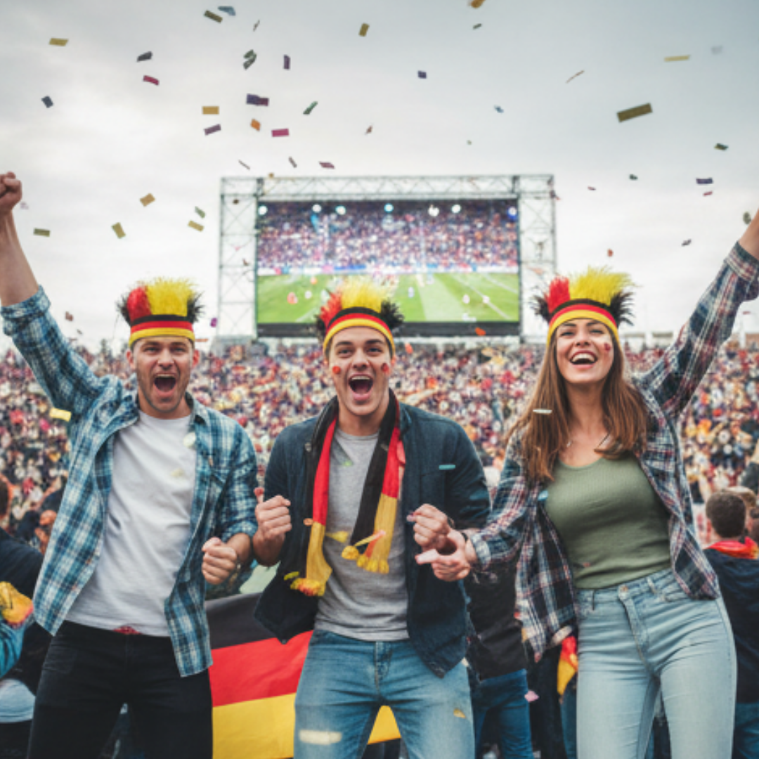 Fans in Deutschland-Trikots jubeln bei einem Fußballspiel, Konfetti fällt.
