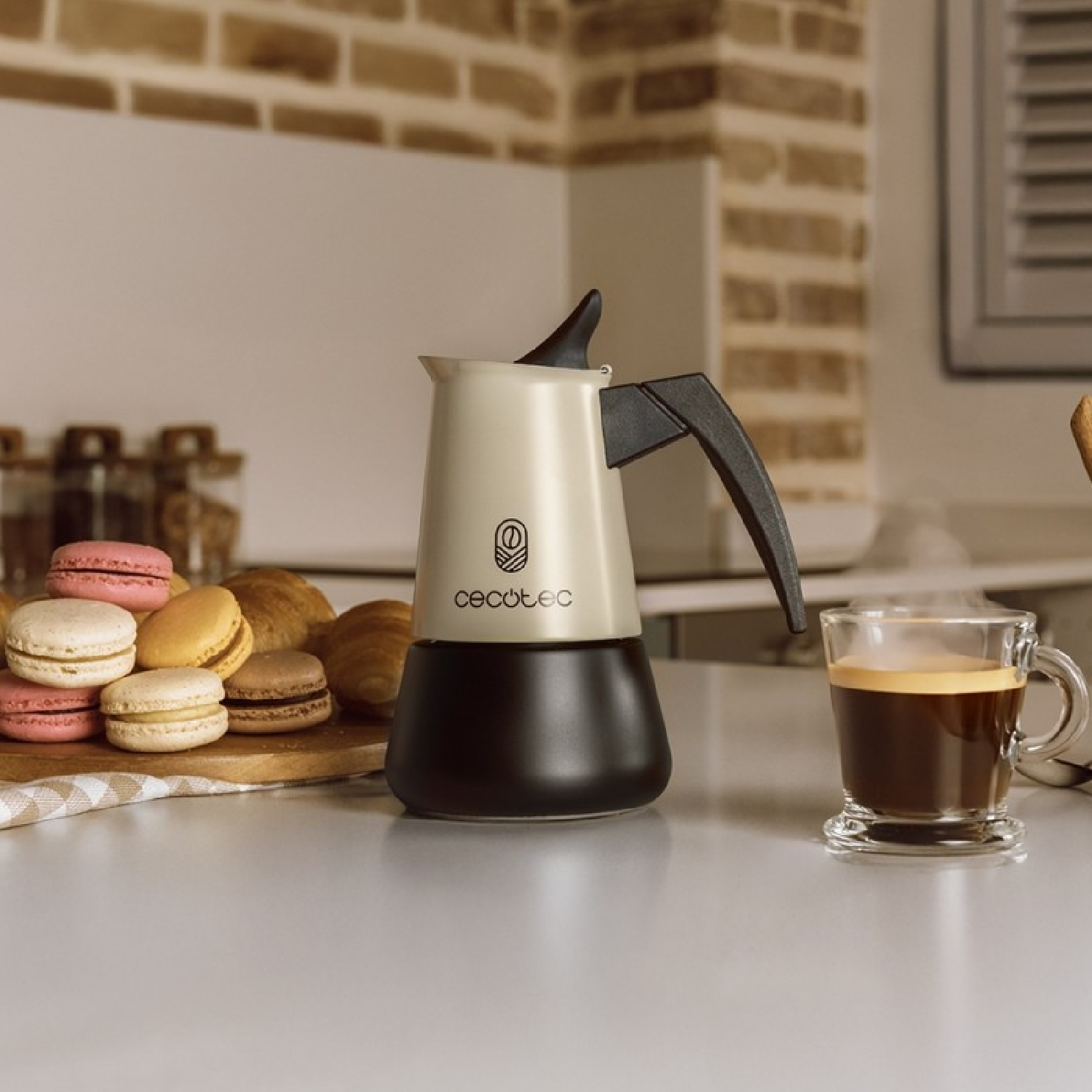 Eine beige Espressokanne mit schwarzem Griff steht neben einer Tasse Kaffee.