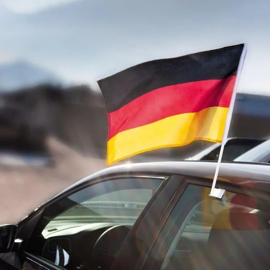 Deutsche Flagge weht auf einem Auto, im Hintergrund unscharfe Landschaft.
