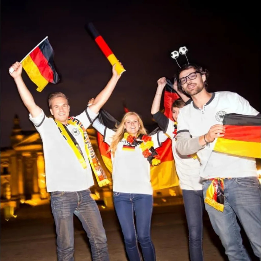 Fans feiern mit Deutschlandflaggen und Schals vor einem Gebäude.