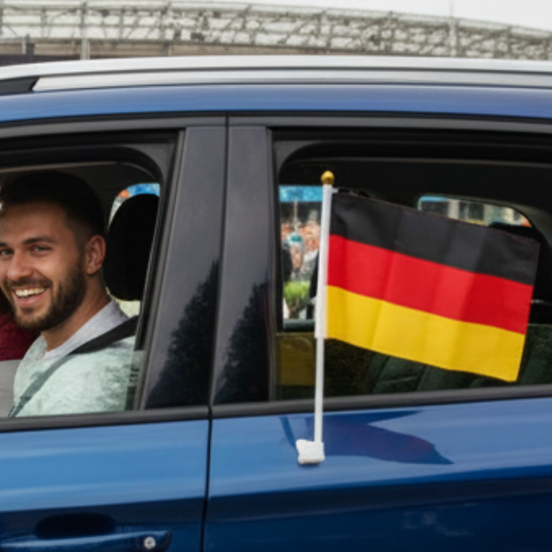 Ein Mann lacht in einem blauen Auto mit einer Deutschlandflagge.