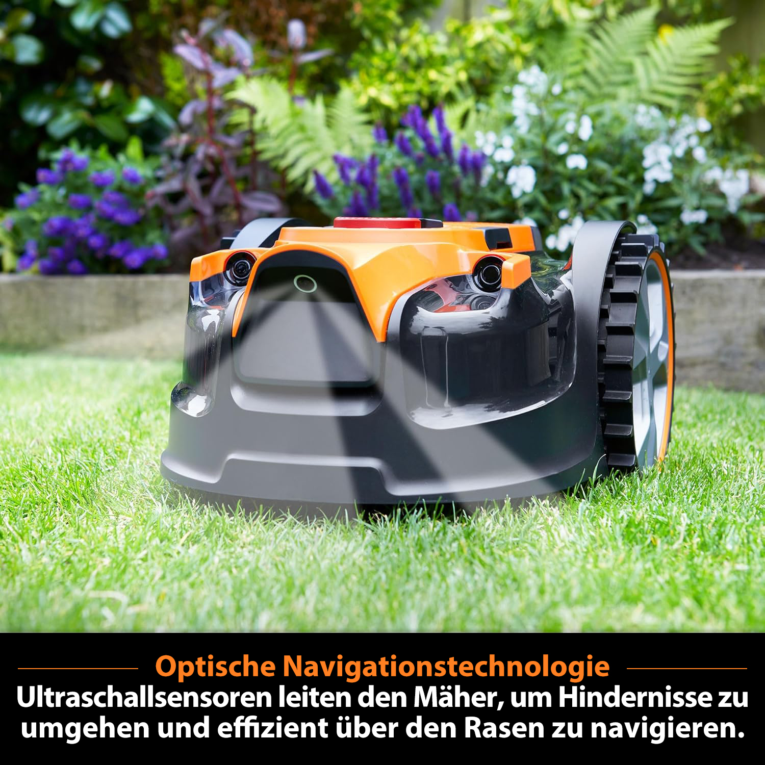 Ein orange-schwarzer Mähroboter auf einem grünen Rasen mit Blumen im Hintergrund.