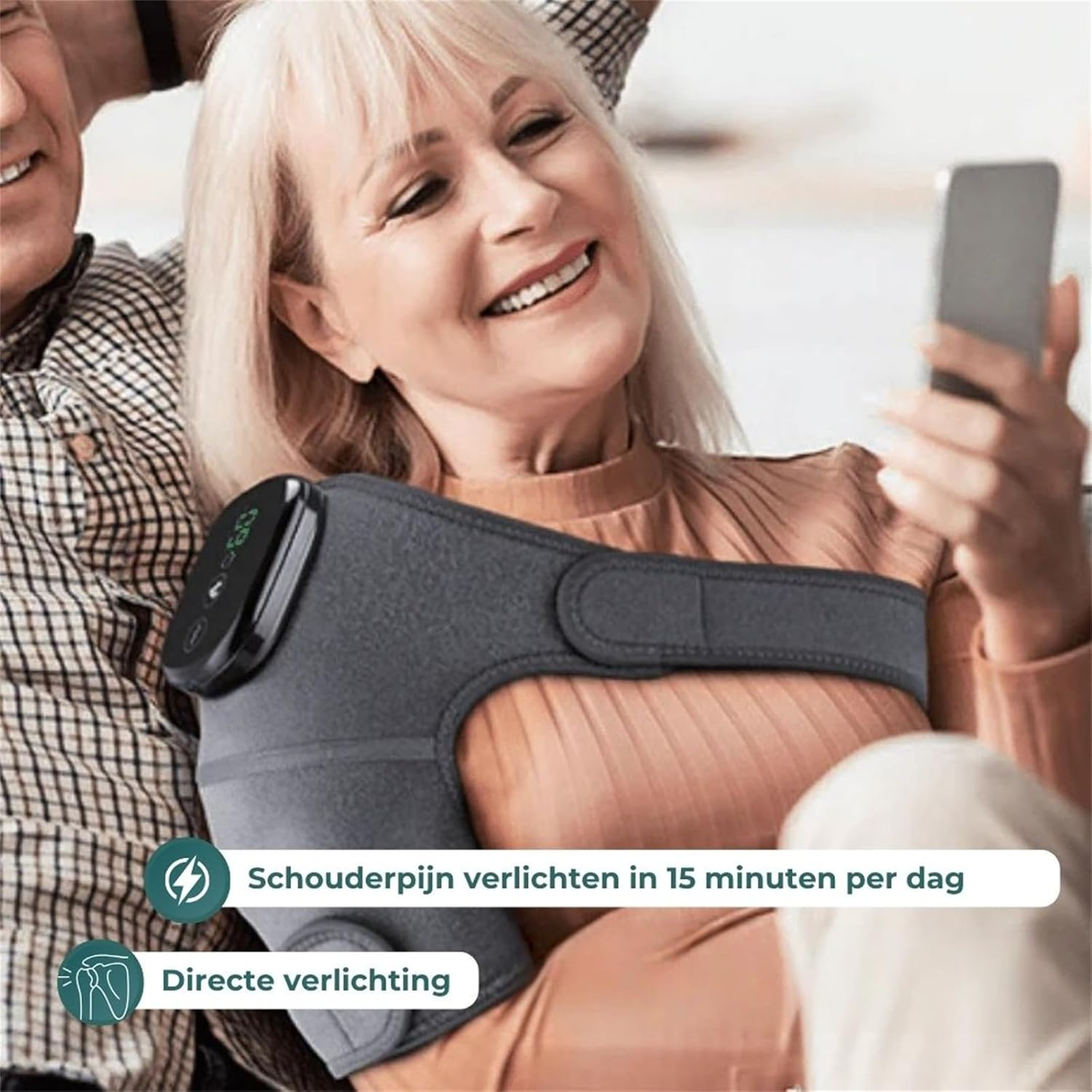 Frau mit Schulterbandage, die ihr Handy benutzt. Ein Mann sitzt daneben.