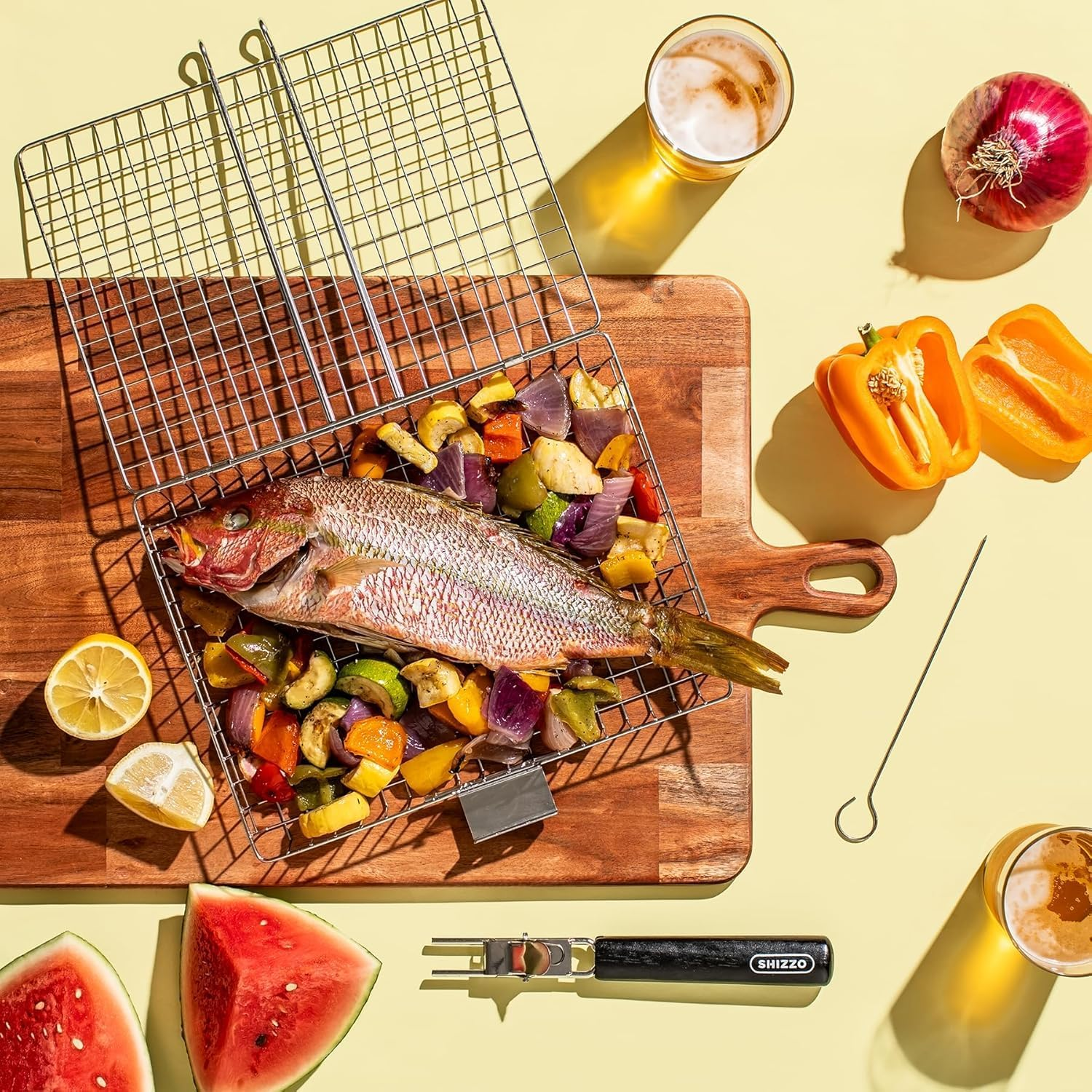 Ganzer Fisch auf Grillrost mit Gemüse, dazu Bier, Zwiebel, Paprika, Zitrone, Wassermelone.