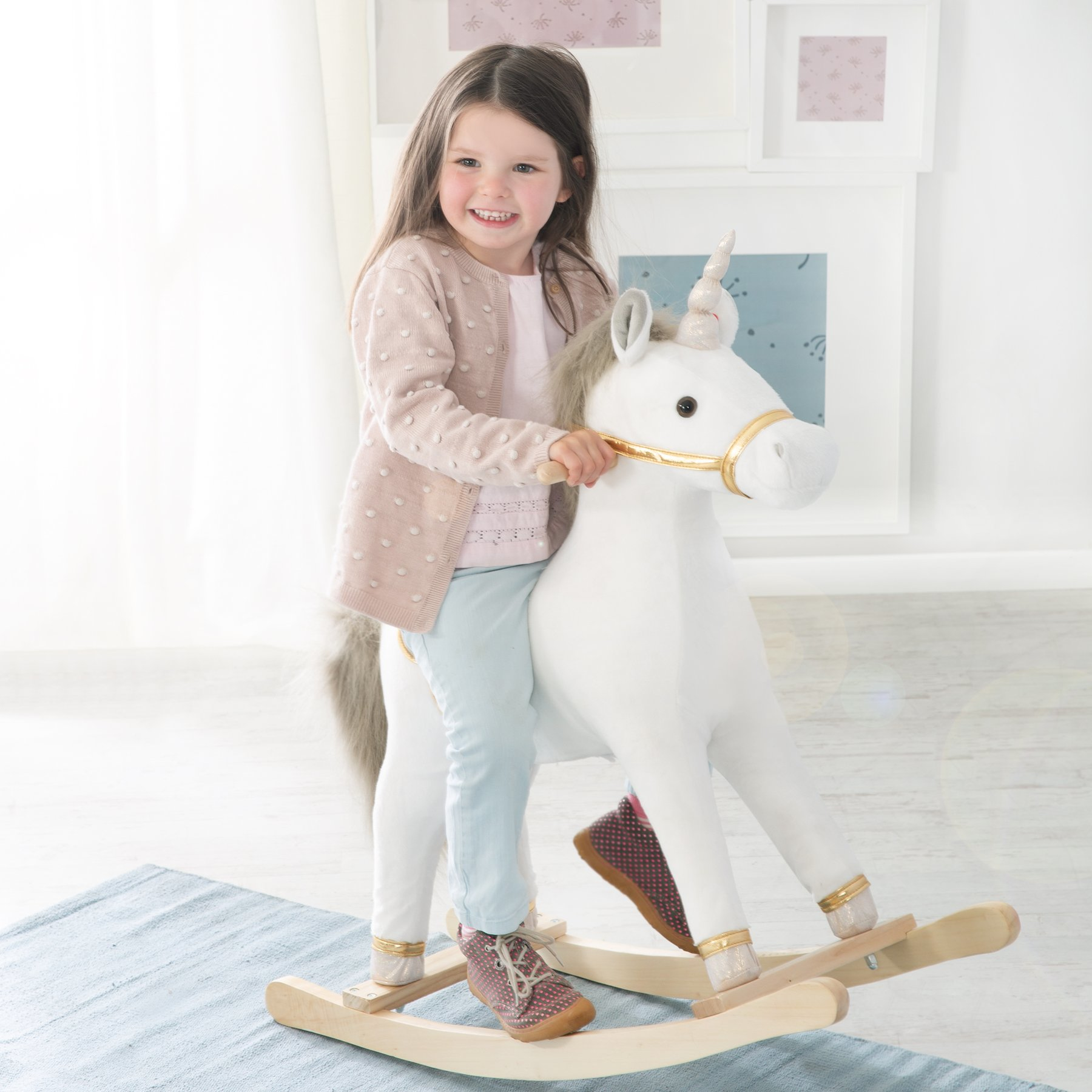 Ein kleines Mädchen reitet auf einem weißen Einhorn-Schaukelpferd vor einem hellen Hintergrund.