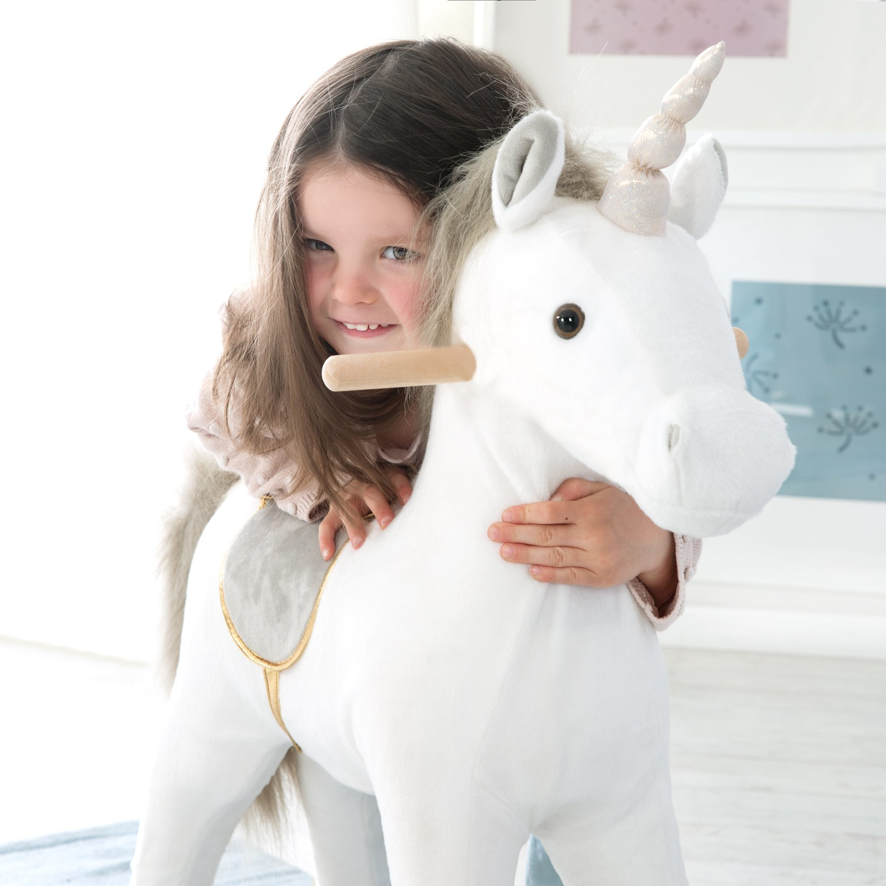Ein kleines Mädchen umarmt ein weißes Plüsch-Einhorn mit goldenen Akzenten.