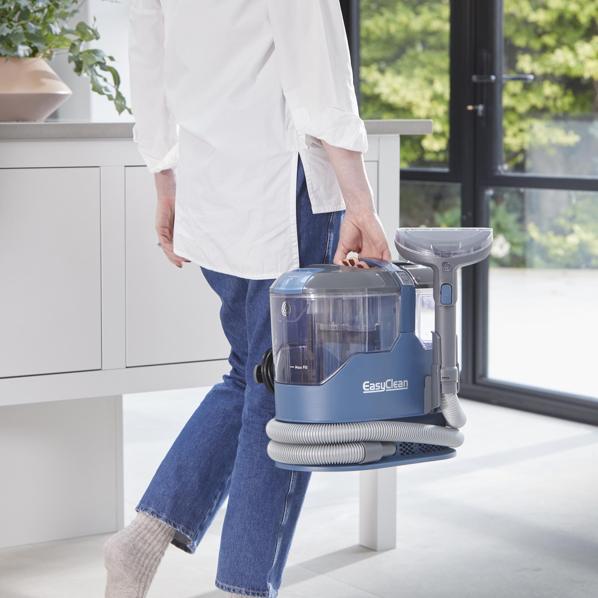 Eine Person trägt einen blauen Teppichreiniger mit Schlauch und Bürste.