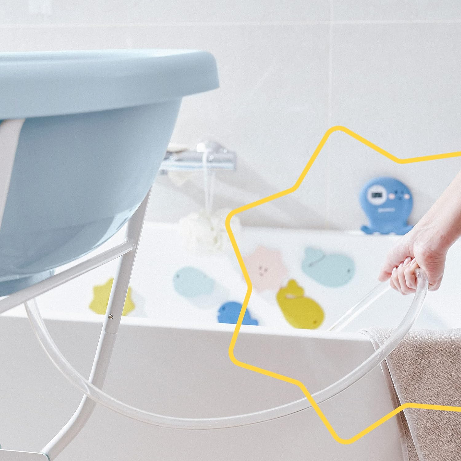 Eine Hand hält einen Schlauch über einer Babybadewanne mit Badespielzeug.