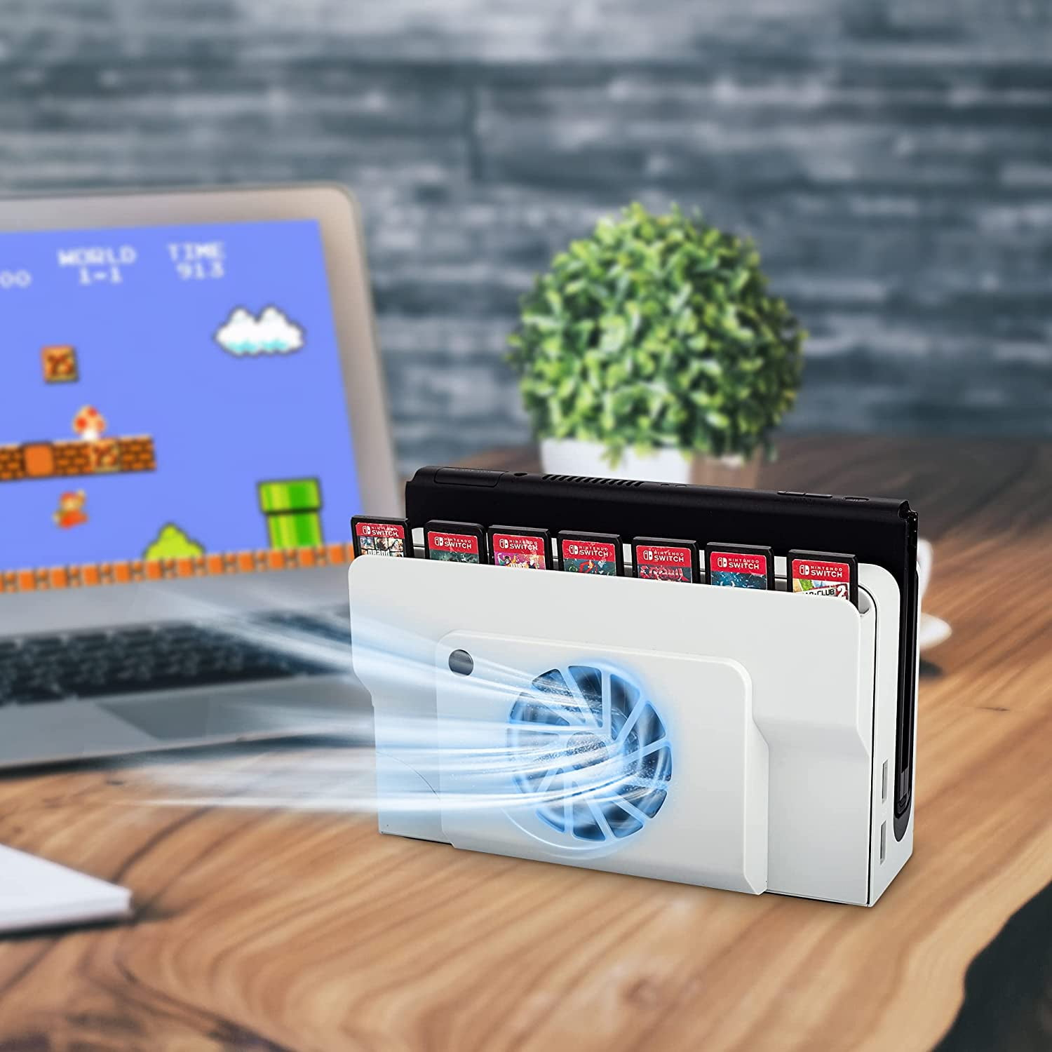 Ein weißer Lüfter kühlt Spielkassetten neben einem Laptop mit einem Videospiel.