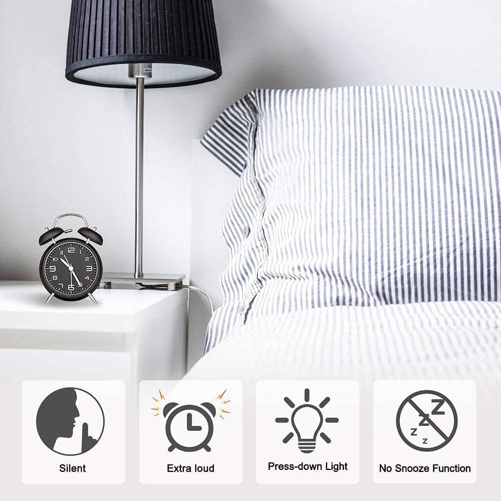 Ein Wecker auf einem Nachttisch neben einem gestreiften Bett und einer Lampe.
