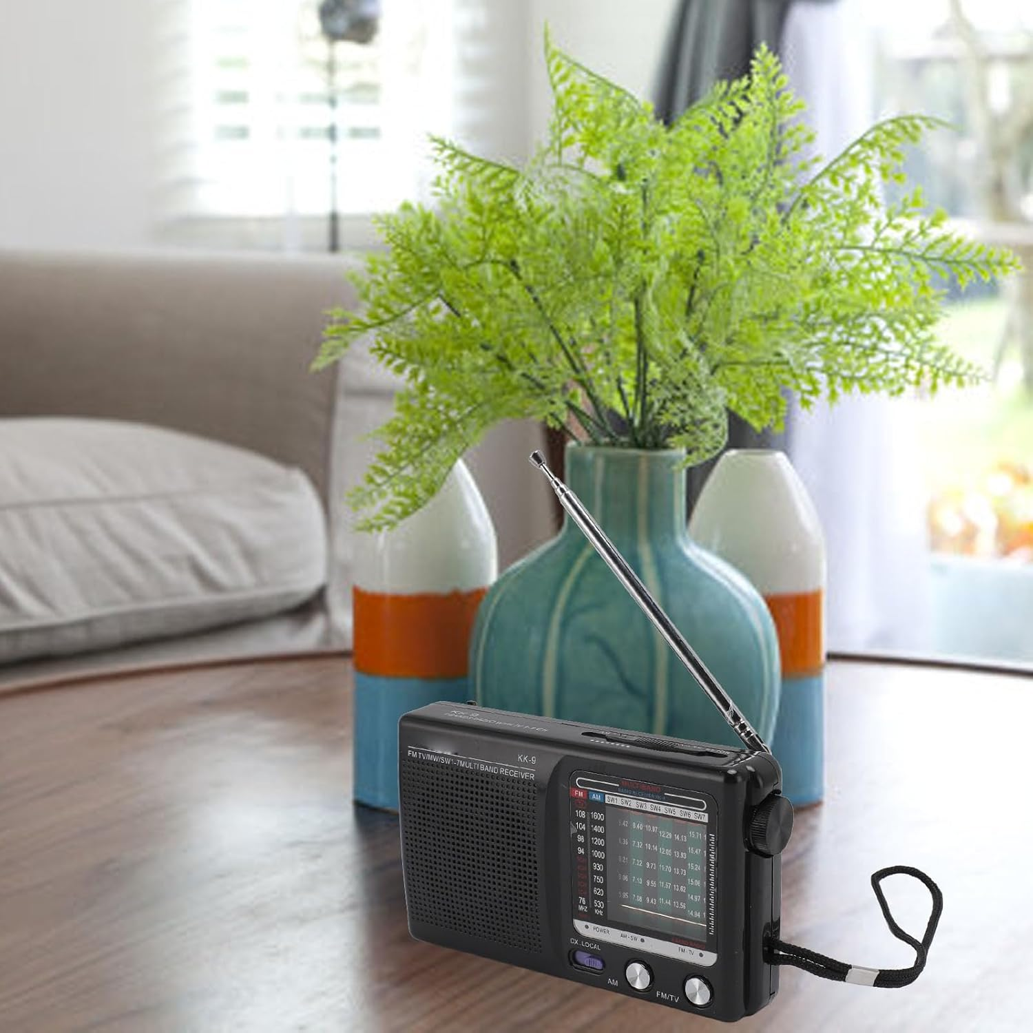 Ein schwarzes Radio mit Antenne steht auf einem Holztisch vor Vasen und Pflanzen.