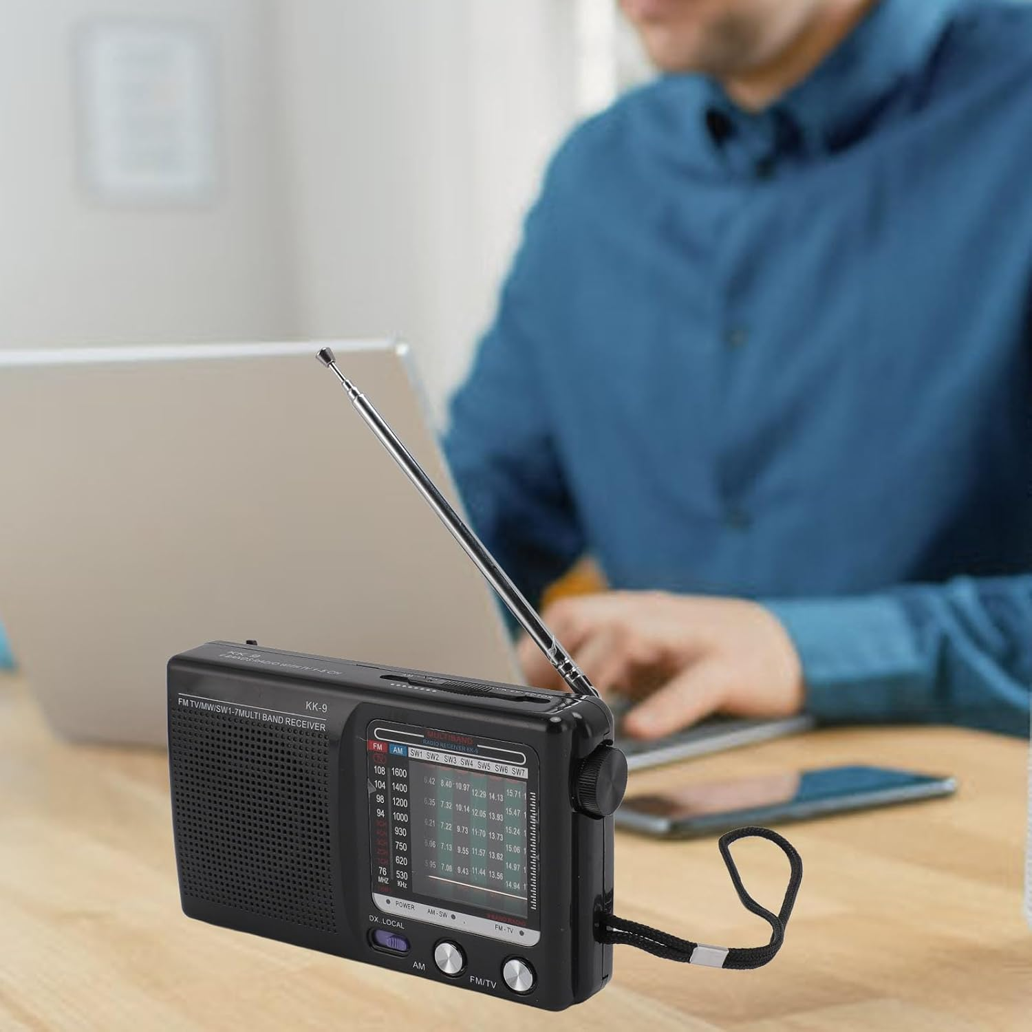 Ein Mann sitzt an einem Tisch und hört über einen schwarzen Radio mit Antenne Musik.