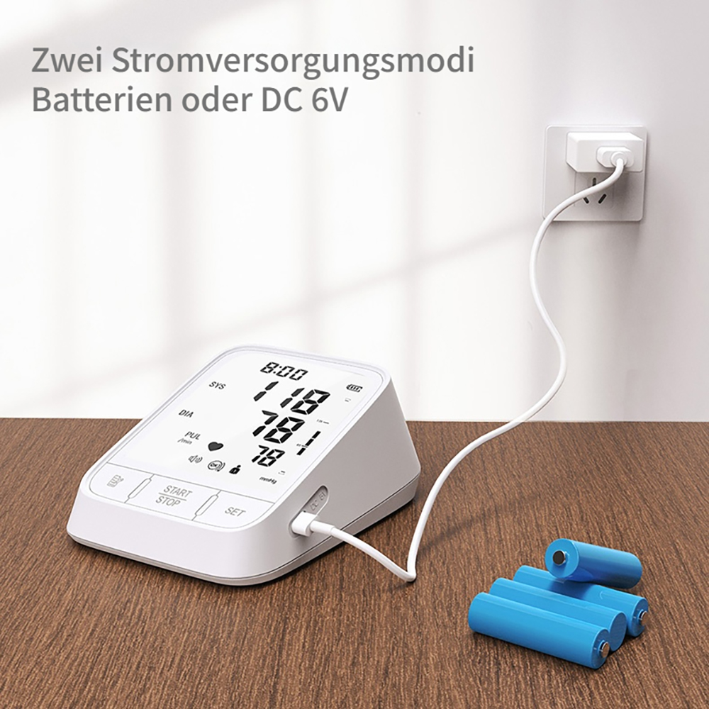 Ein weißes Blutdruckmessgerät ist mit einem Netzteil verbunden. Drei Batterien liegen daneben.