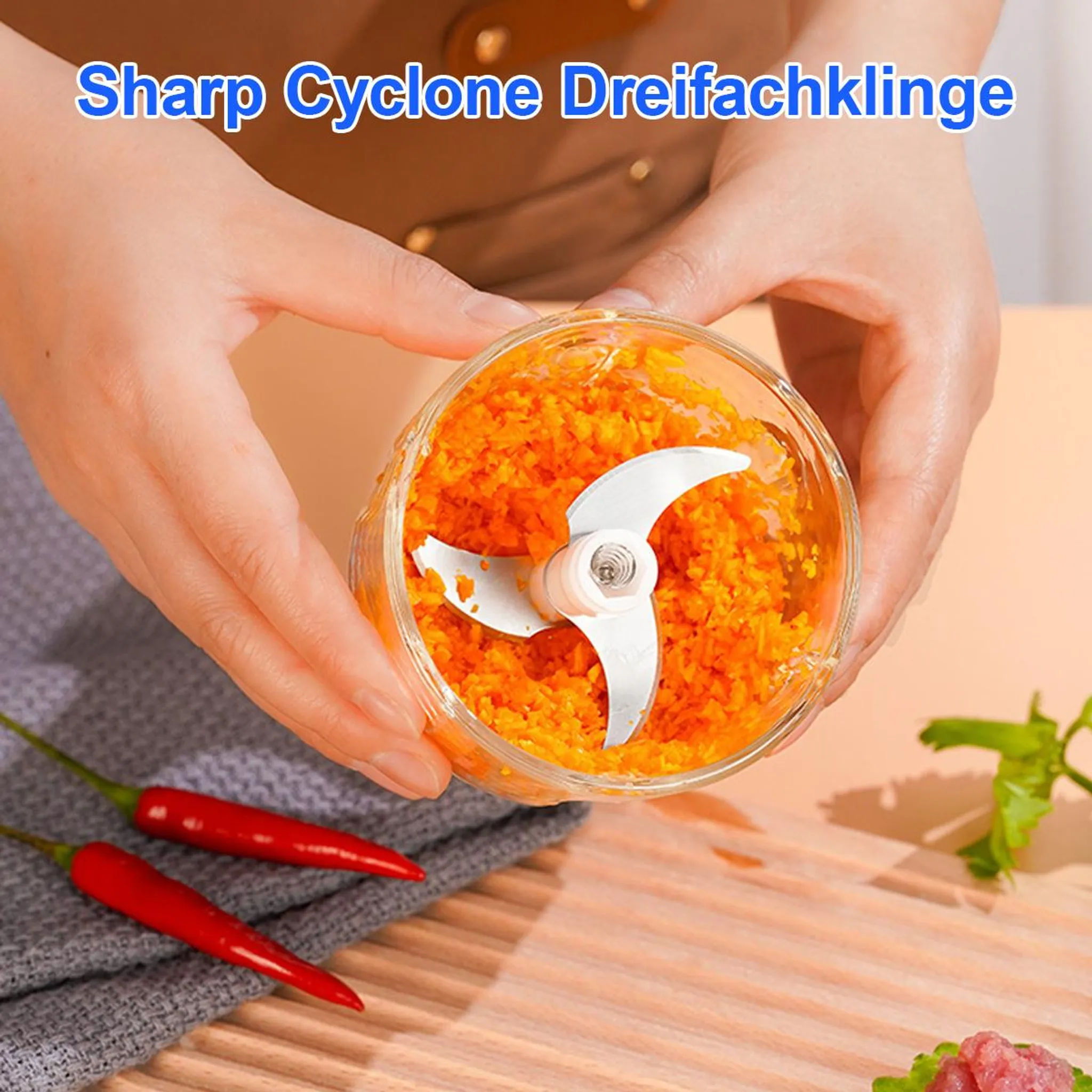 Hände halten einen Zerkleinerer mit Karotten, daneben Chilis.