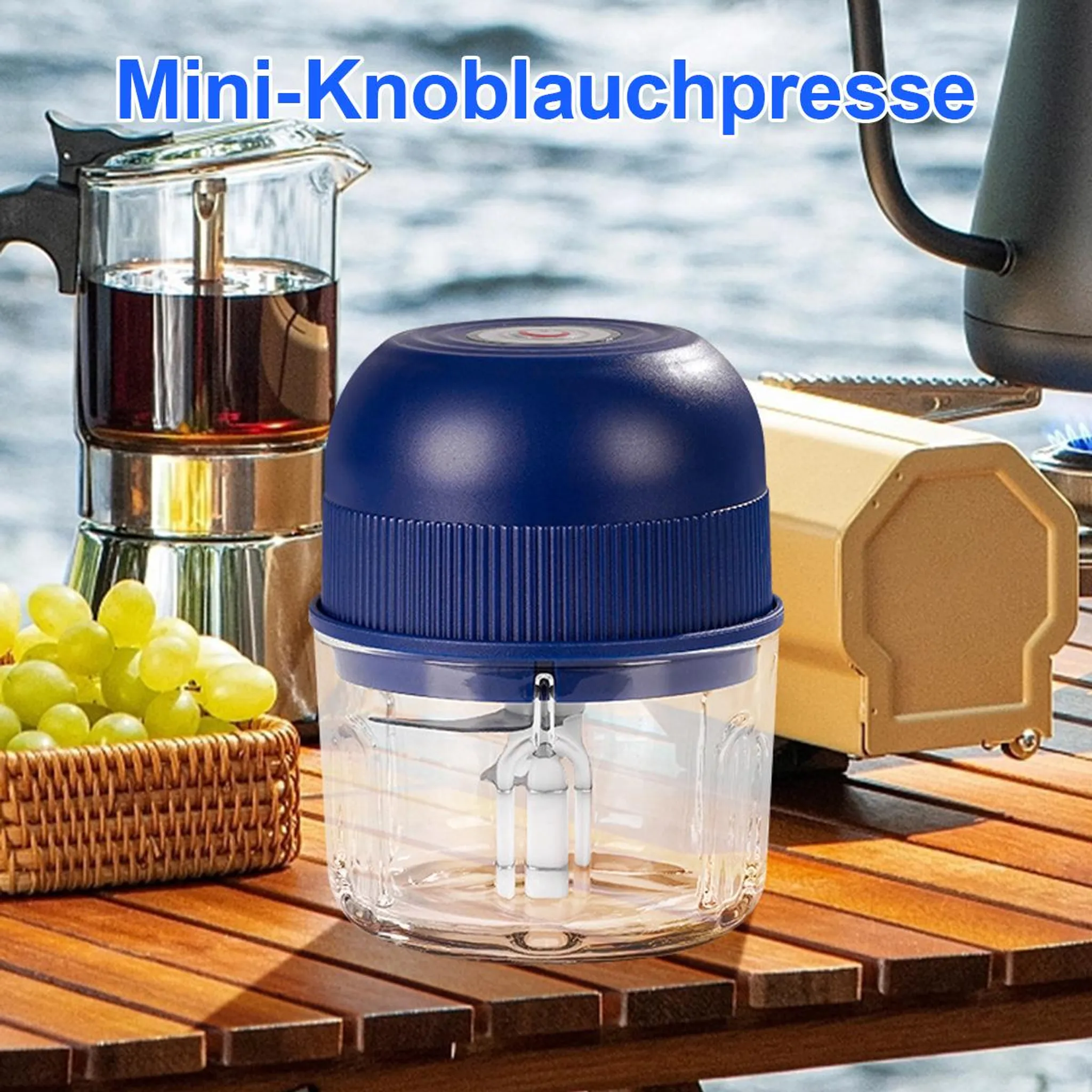 Ein blauer Mini-Knoblauchzerkleinerer steht auf einem Holztisch neben einer Kaffeekanne und Trauben.