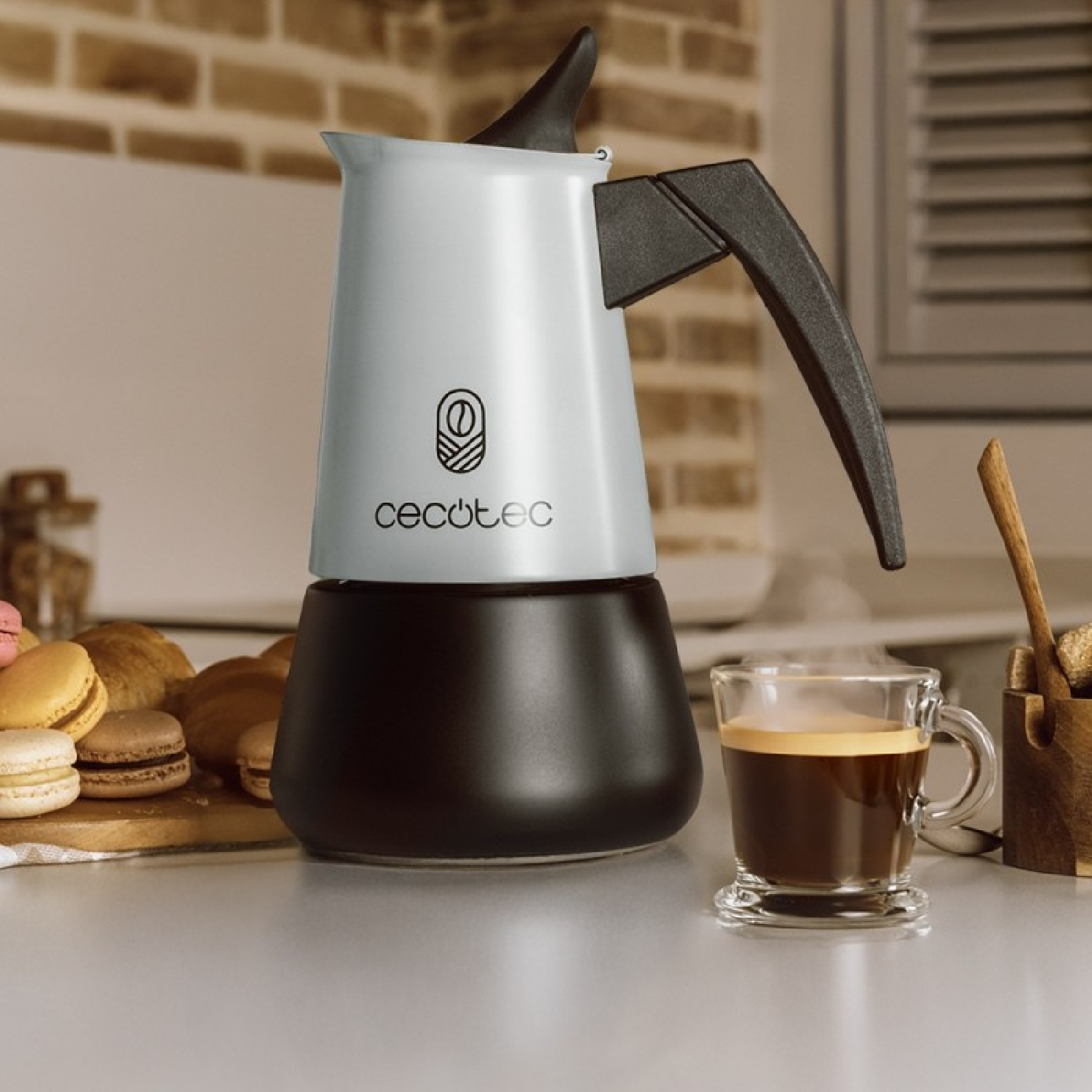 Una moka bianca emana vapore accanto a un bicchiere di caffè, con macarons e croissant vicini.