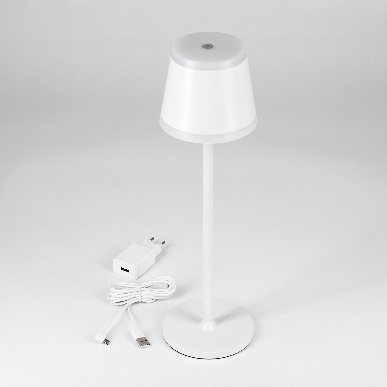 Eine weiße Nachttischlampe mit Ladegerät und USB-Kabel auf weißem Hintergrund.