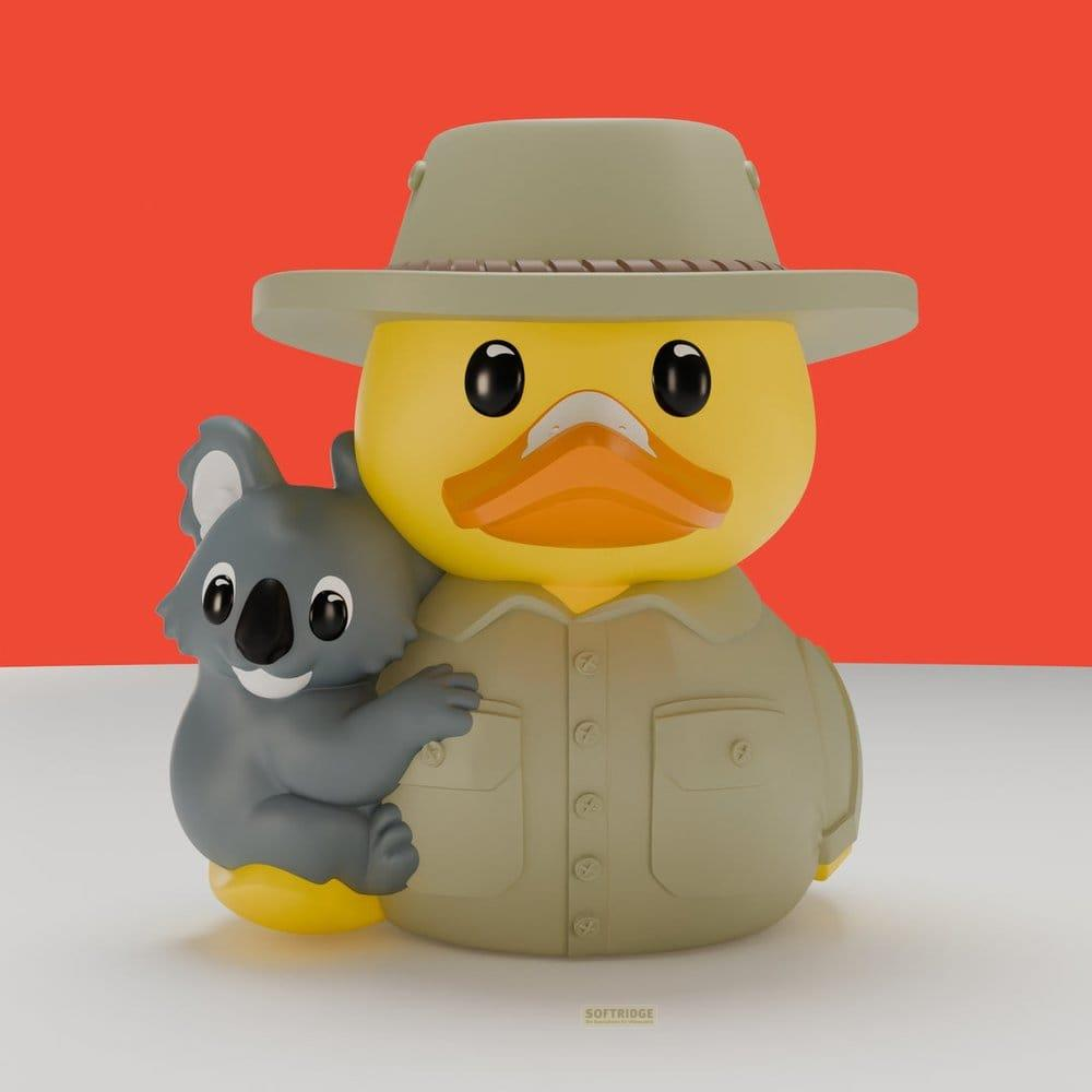 Eine gelbe Gummi-Ente im Safari-Outfit mit einem Koala auf dem Arm vor rotem Hintergrund.