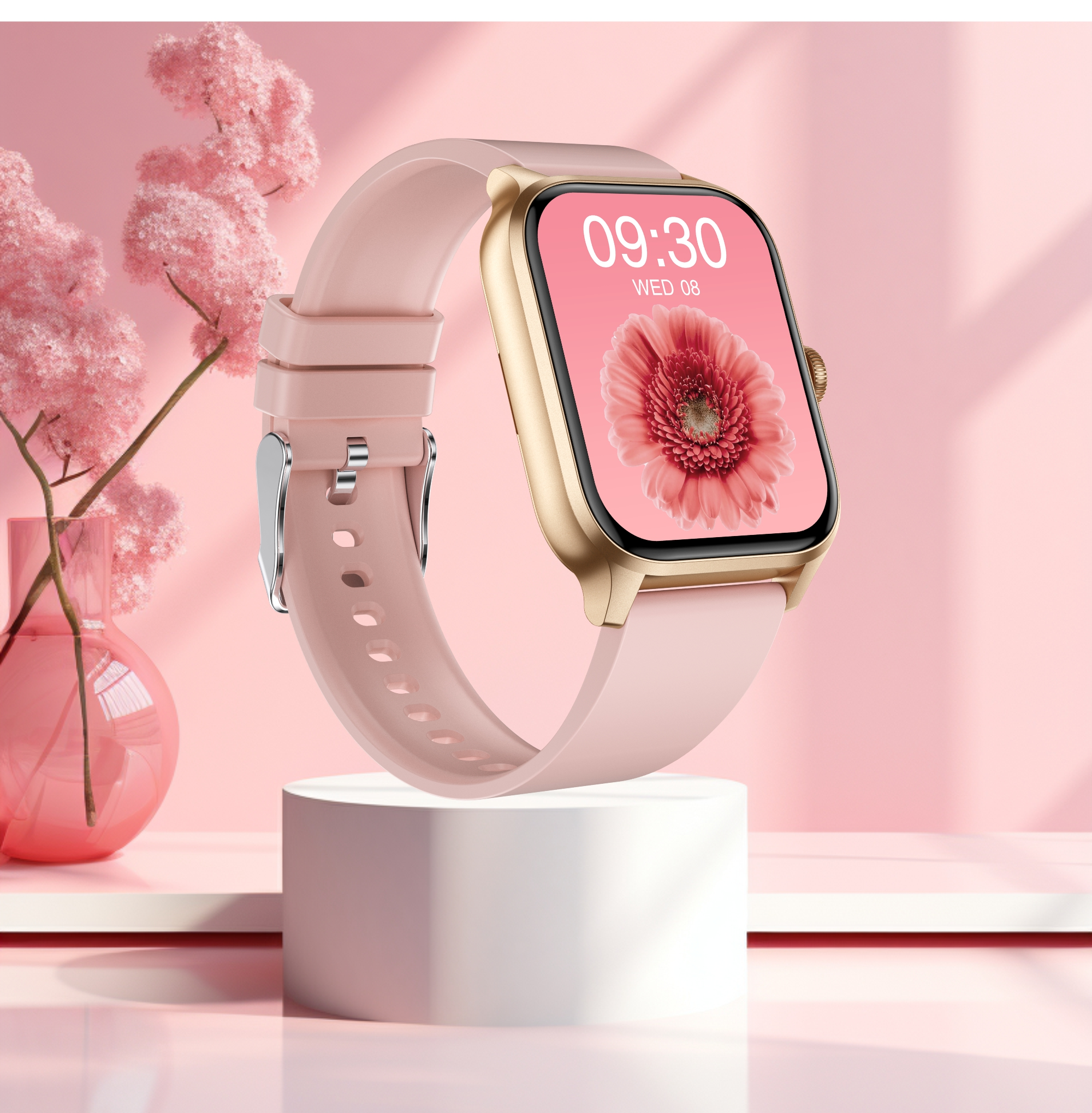 Eine rosafarbene Smartwatch mit goldenem Gehäuse auf einem weißen Podest. Links eine Vase mit rosa Blumen.