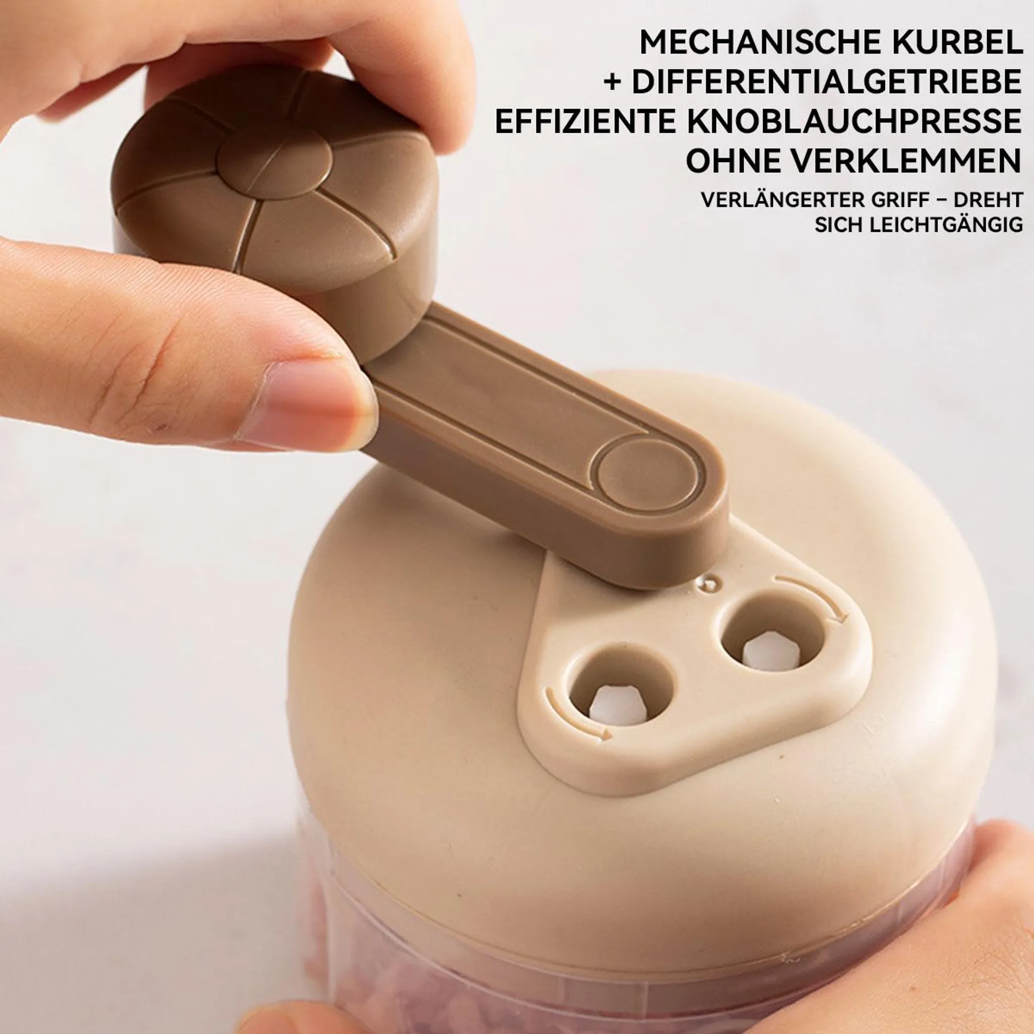Eine Hand dreht den Kurbelgriff eines beigen Knoblauchpressers über einem transparenten Behälter.