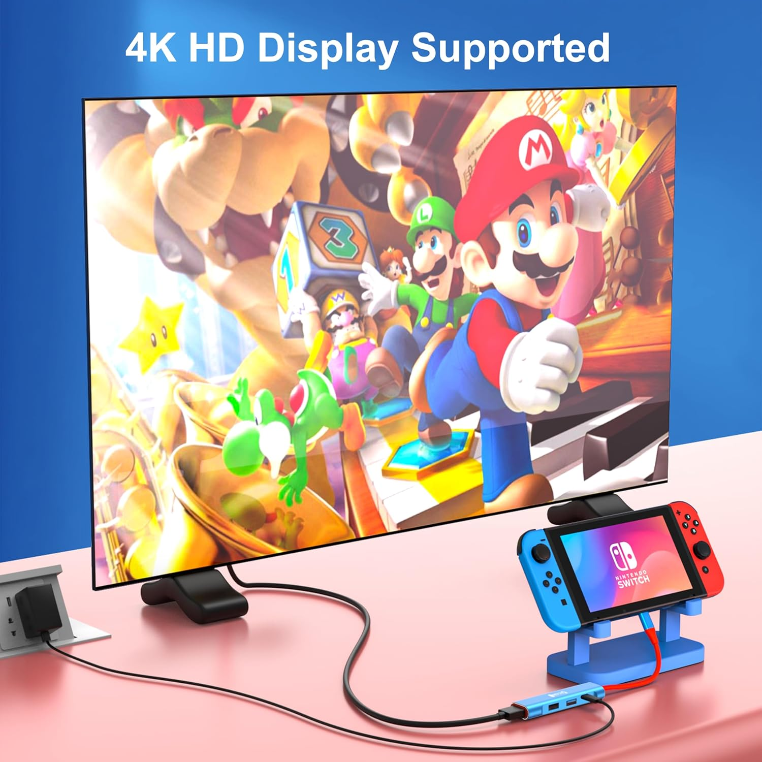 Nintendo Switch an 4K-Display mit Mario-Figuren angeschlossen. Zubehör auf rosa Unterlage.