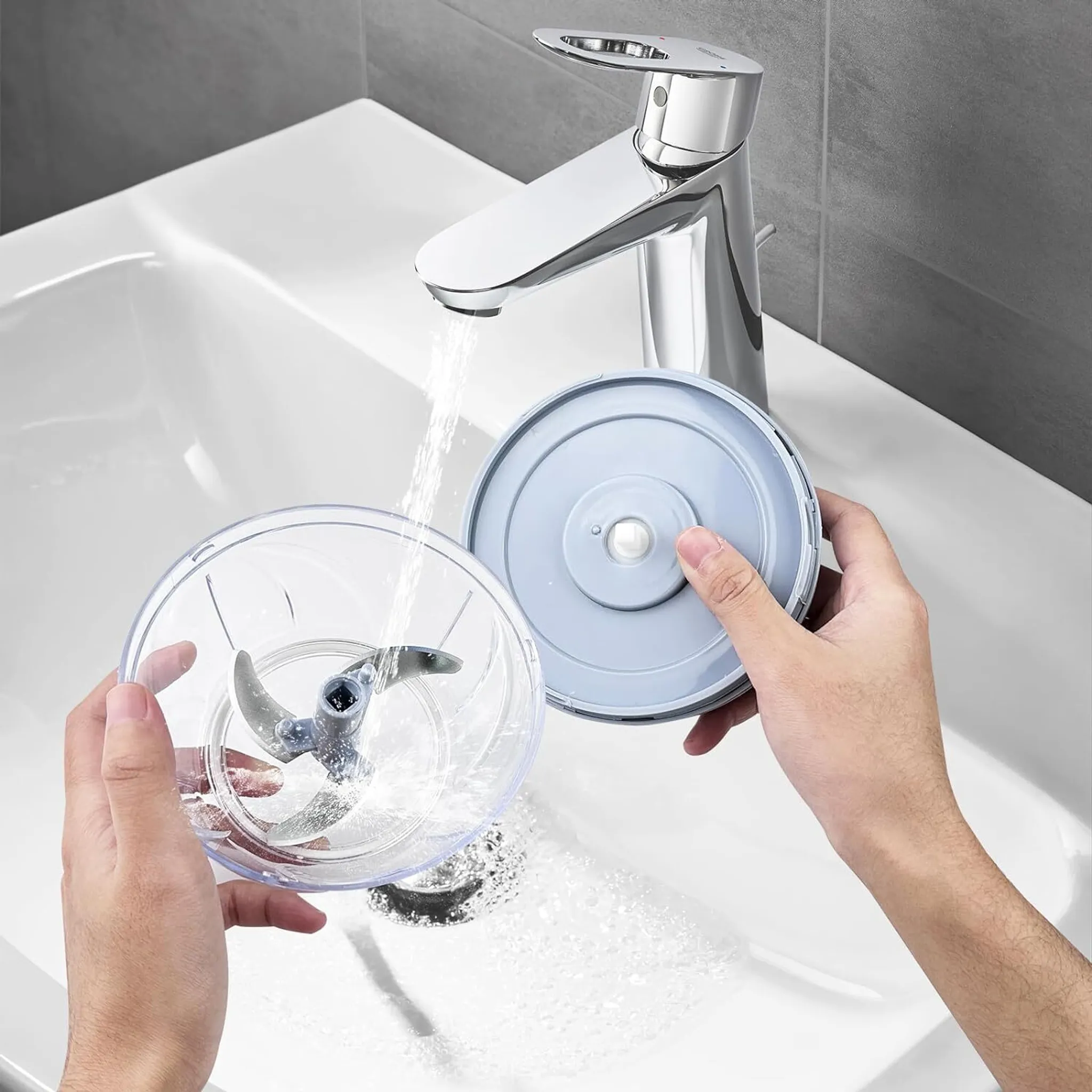 Hände reinigen einen transparenten Behälter mit Klingen unter fließendem Wasser in einem Waschbecken.