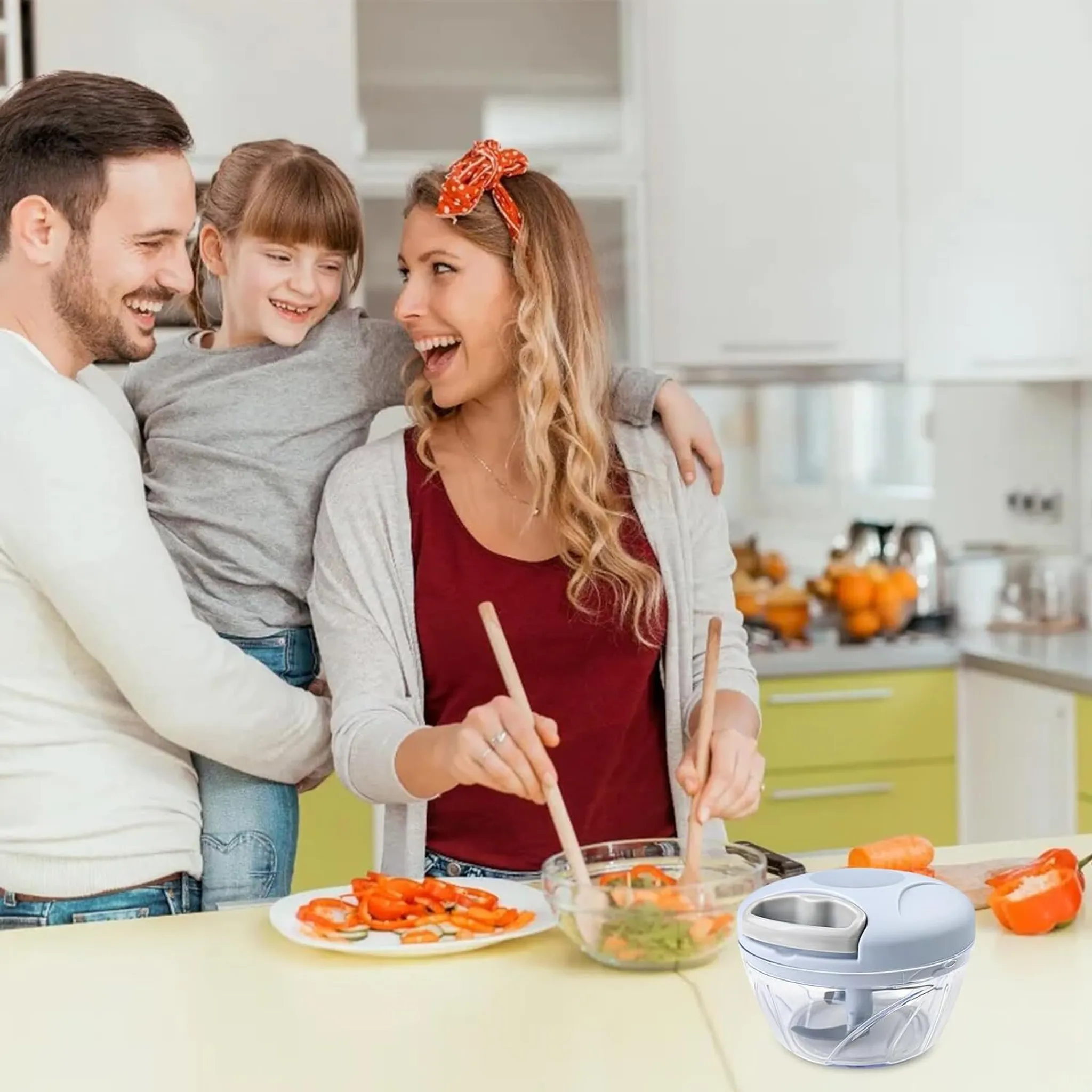 Familie bereitet Essen in der Küche zu; Mann hält Kind, Frau rührt Salat.