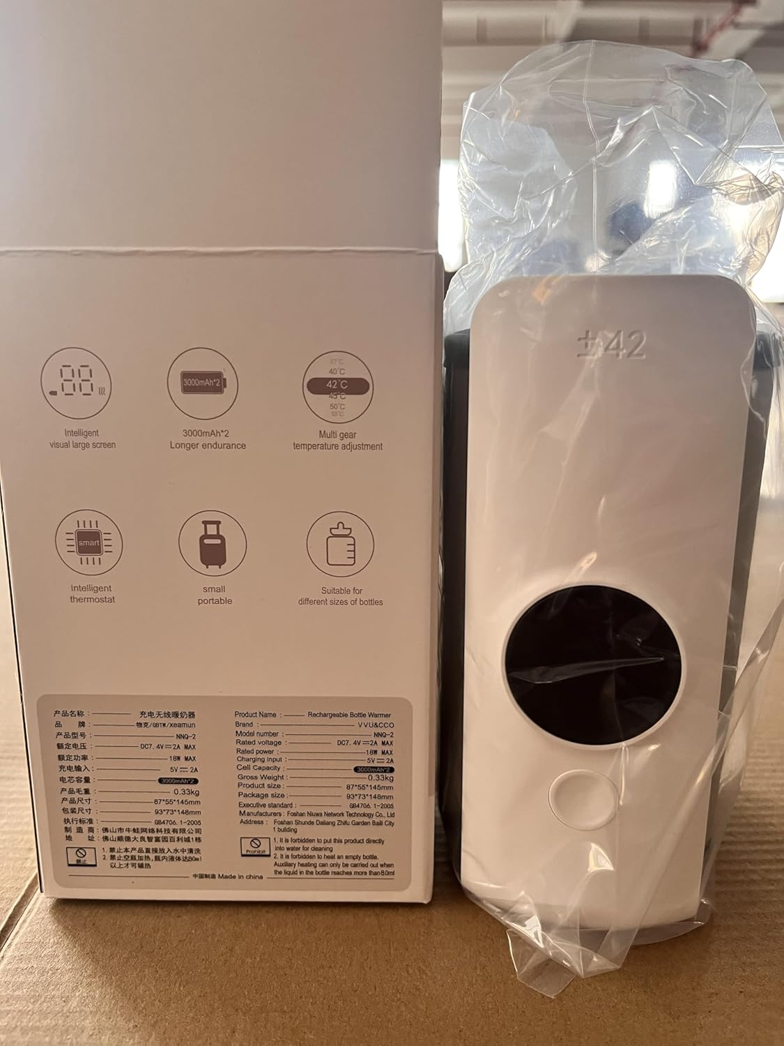 Ein weißer wiederaufladbarer Flaschenwärmer mit #42-Logo, daneben eine offene Verpackung mit Produktinformationen.