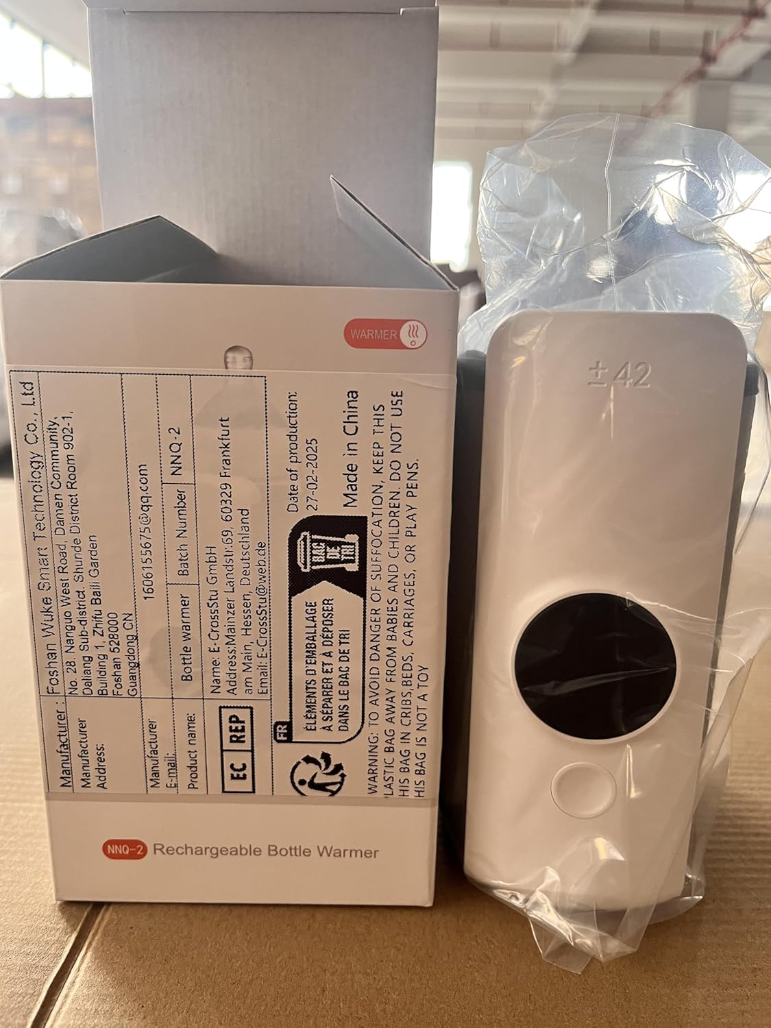 Ein weißer Flaschenwärmer mit schwarzem Kreisdisplay auf einem Karton mit Produktinformationen.