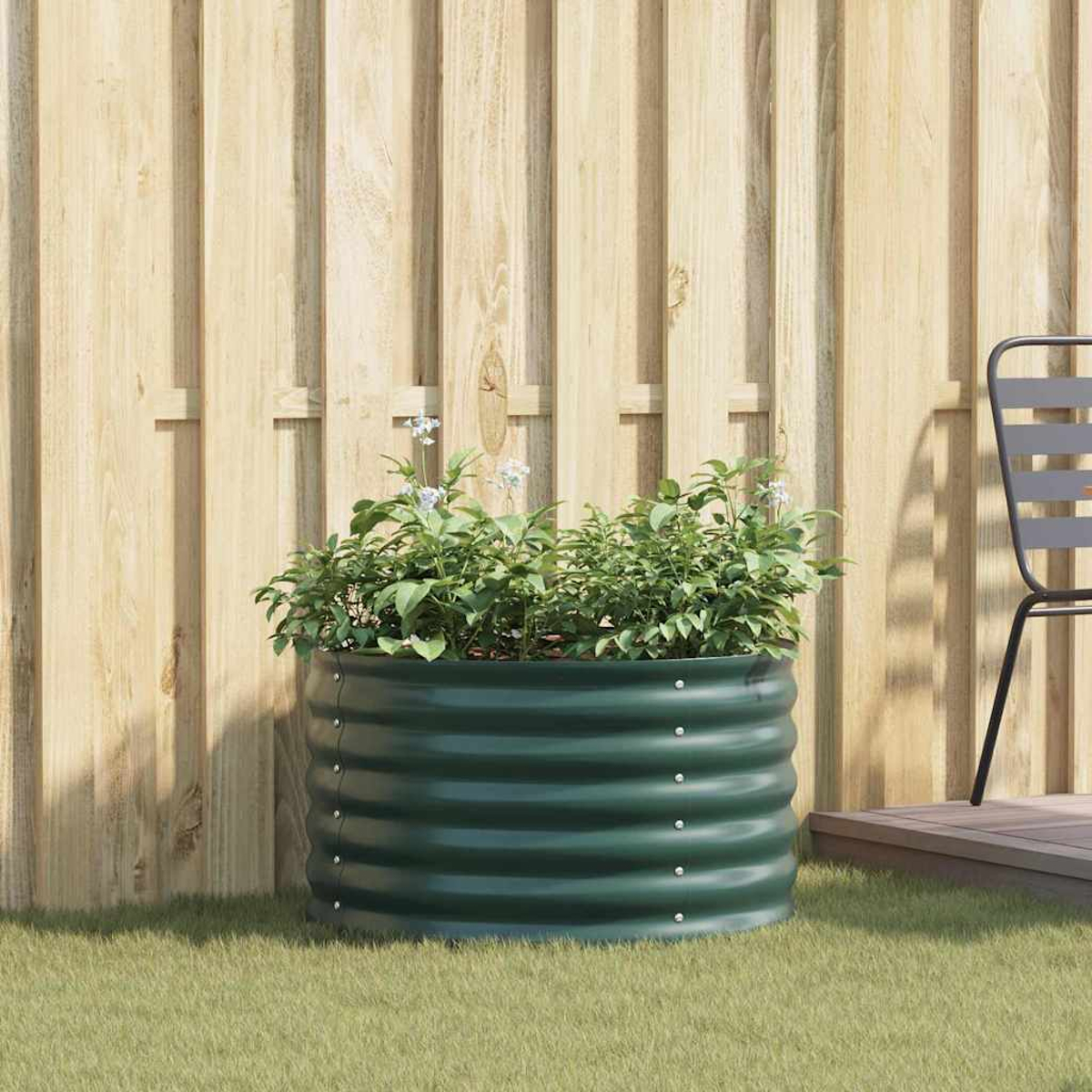 Fioriera rialzata verde con piante davanti a una recinzione di legno.