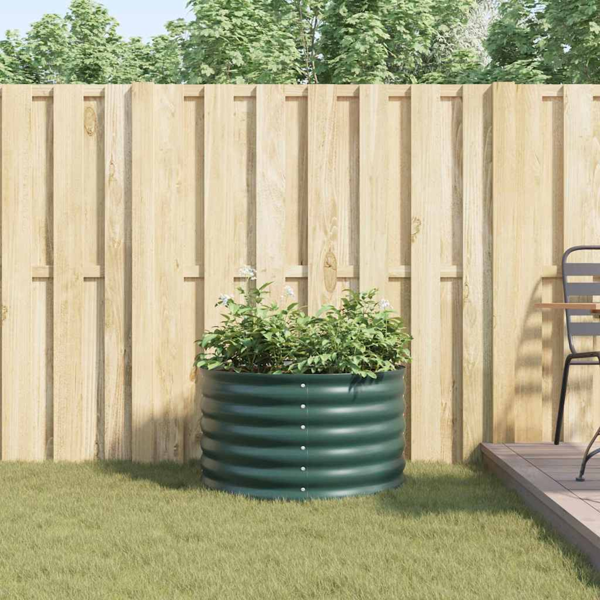 Un fioriera rialzata verde con piante verdi siede sull'erba davanti a una recinzione di legno.