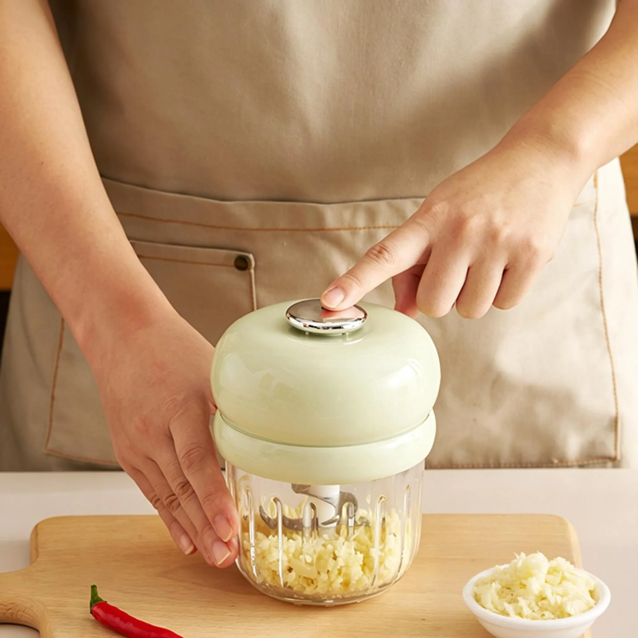 Eine Person benutzt einen kleinen, hellgrünen Garlic Chopper mit einem Glasbehälter voller gehacktem Knoblauch.