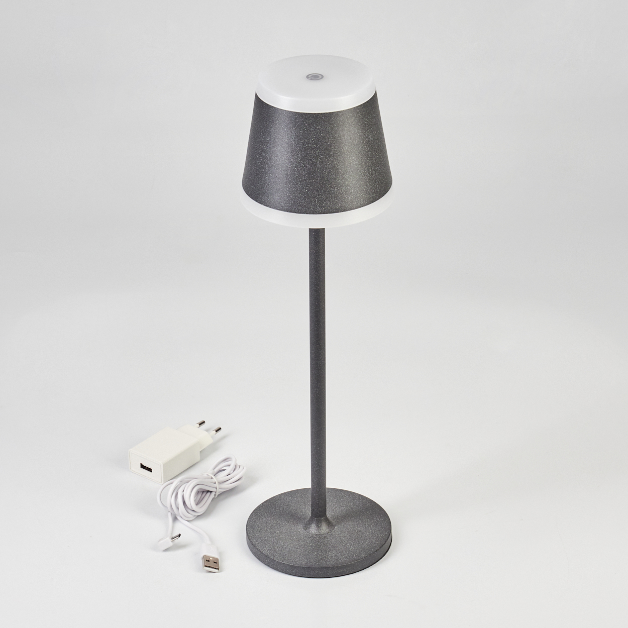 Graue Lampe mit weißem Schirm, Ladekabel und weißem Netzstecker.