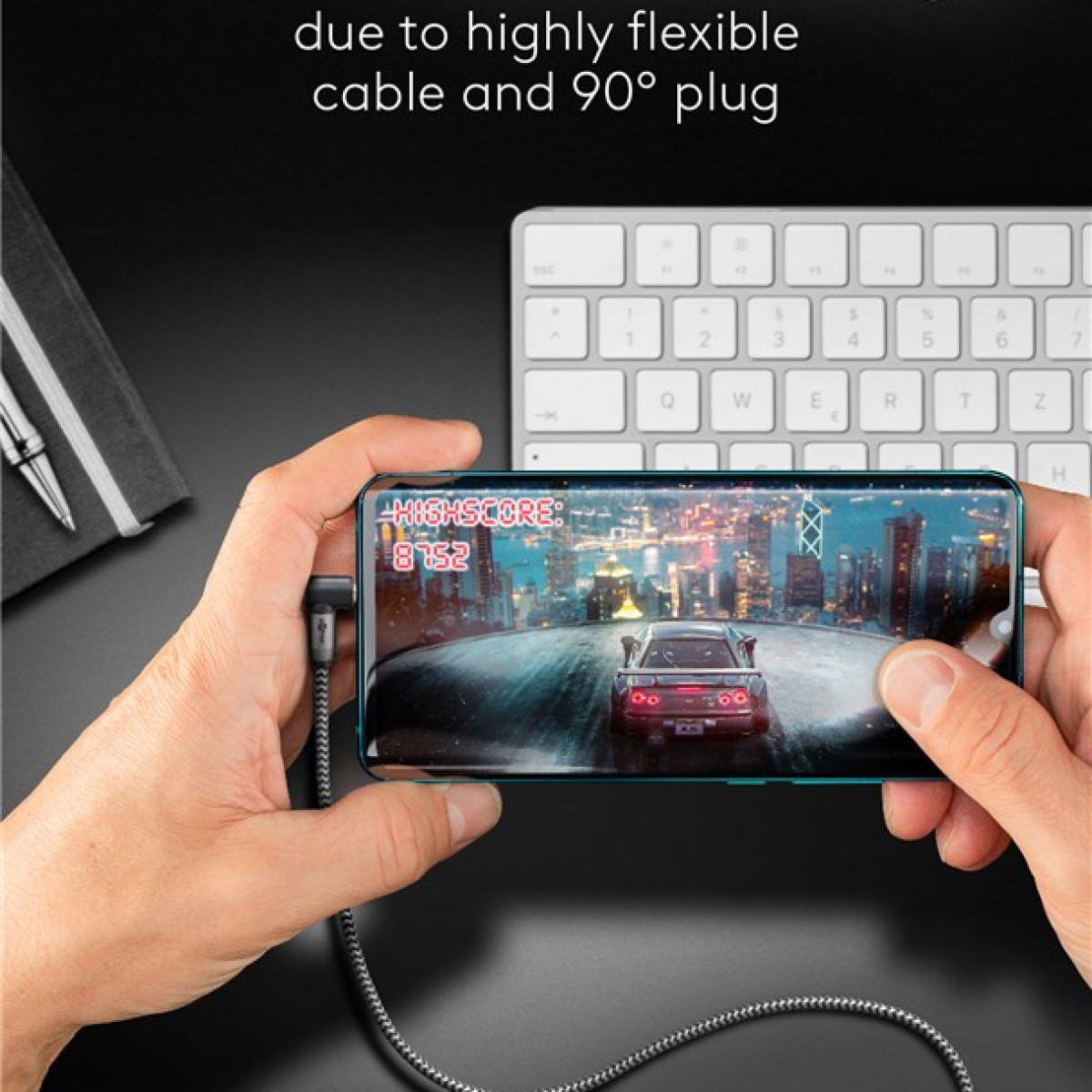 Hände halten Handy mit Rennspiel, Laptop-Tastatur im Hintergrund.