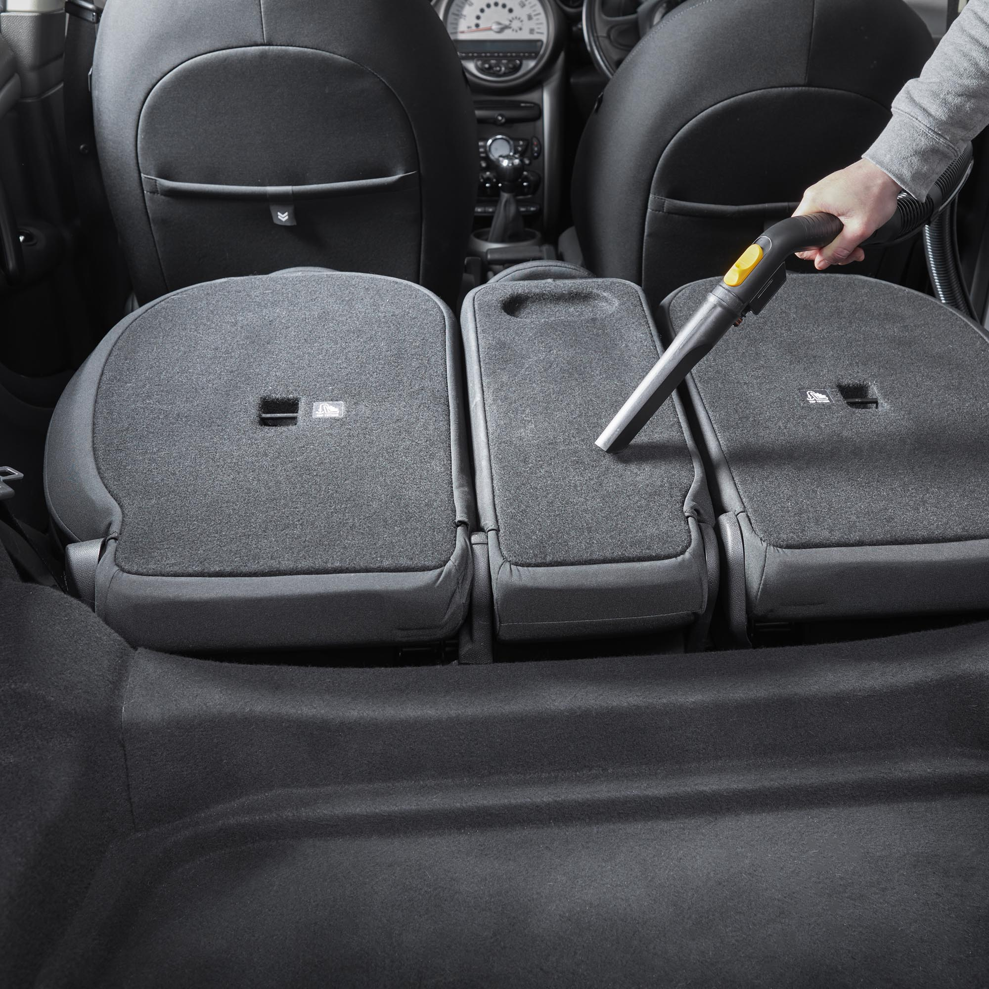 Eine Hand benutzt einen Staubsauger, um den Rücksitz eines Autos zu reinigen.