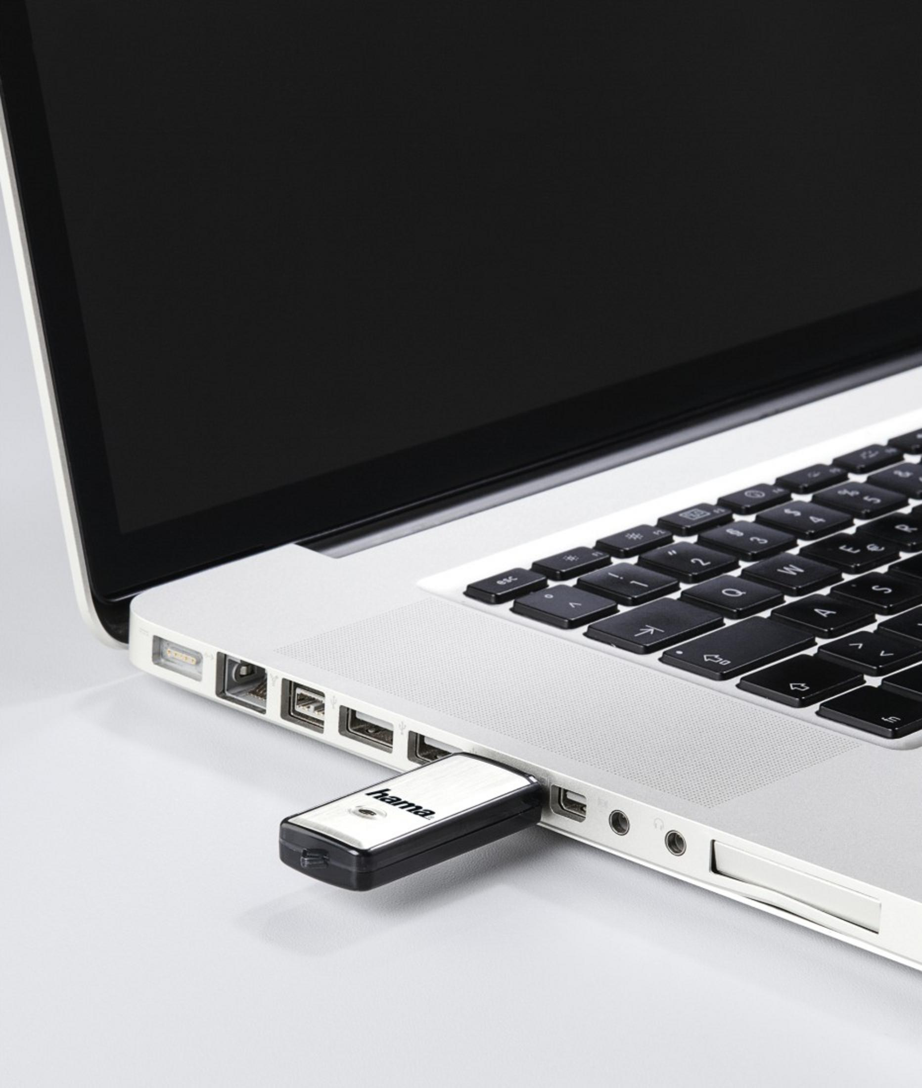 Ein weißer USB-Stick mit schwarzer Zierleiste ist in einen silbernen Laptop eingesteckt.