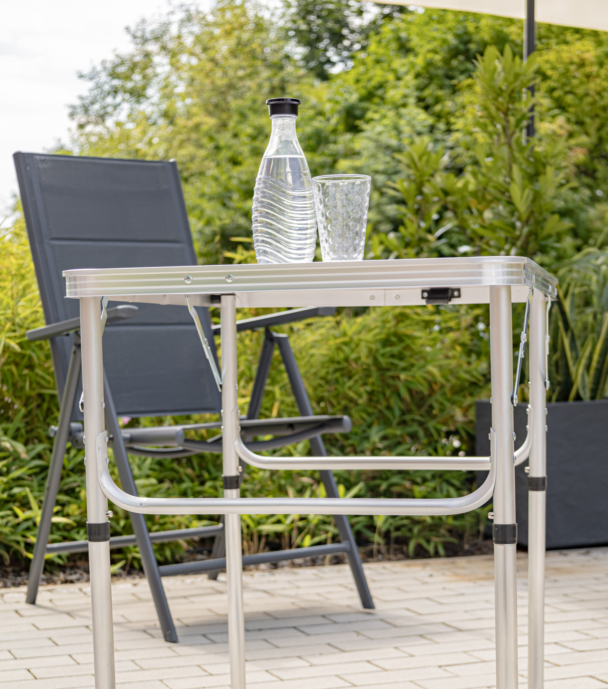 Ein Tisch mit Wasserflasche und Glas steht auf einer Terrasse neben einem Stuhl.