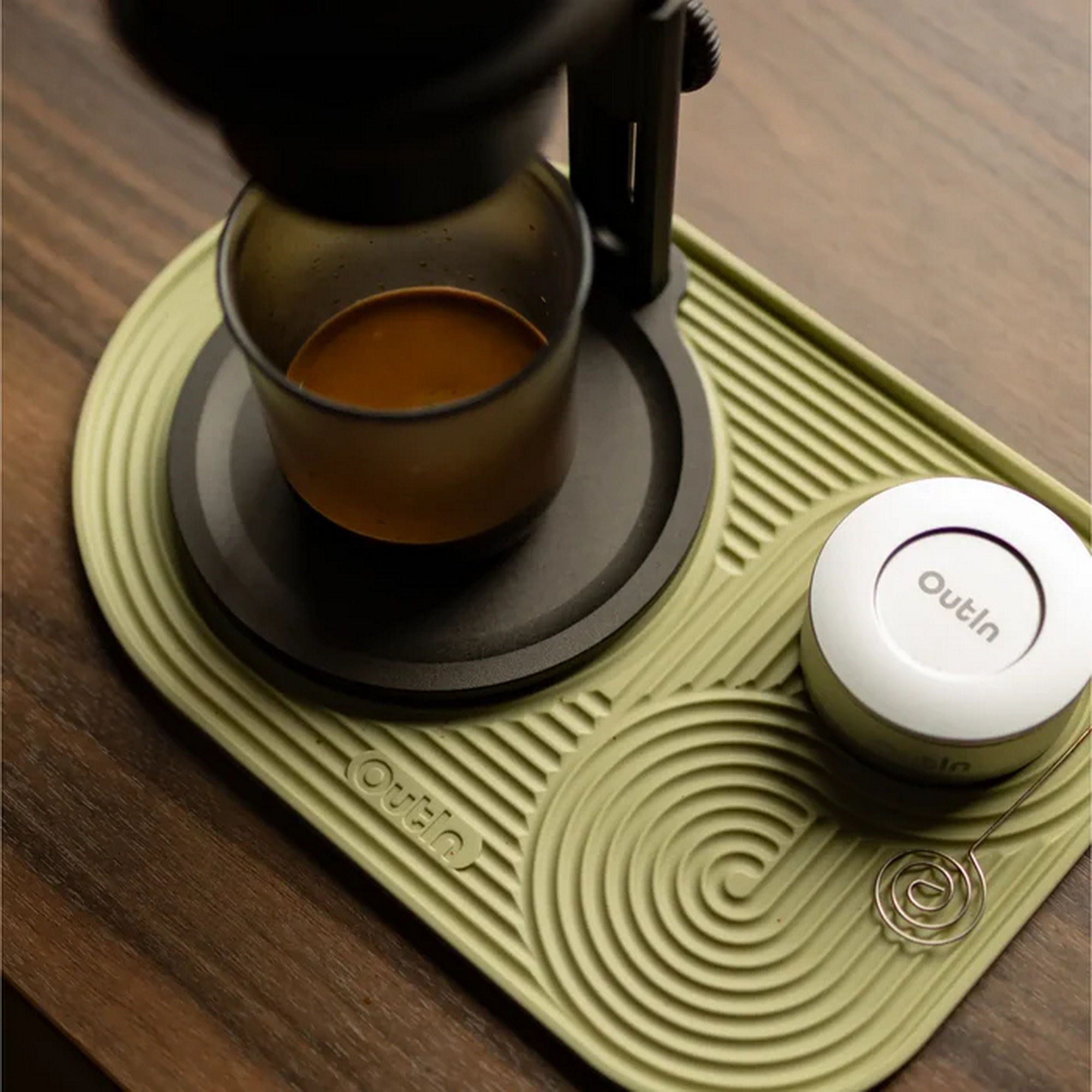 Een espressomachine zet koffie in een glas op een lichtgroene mat.