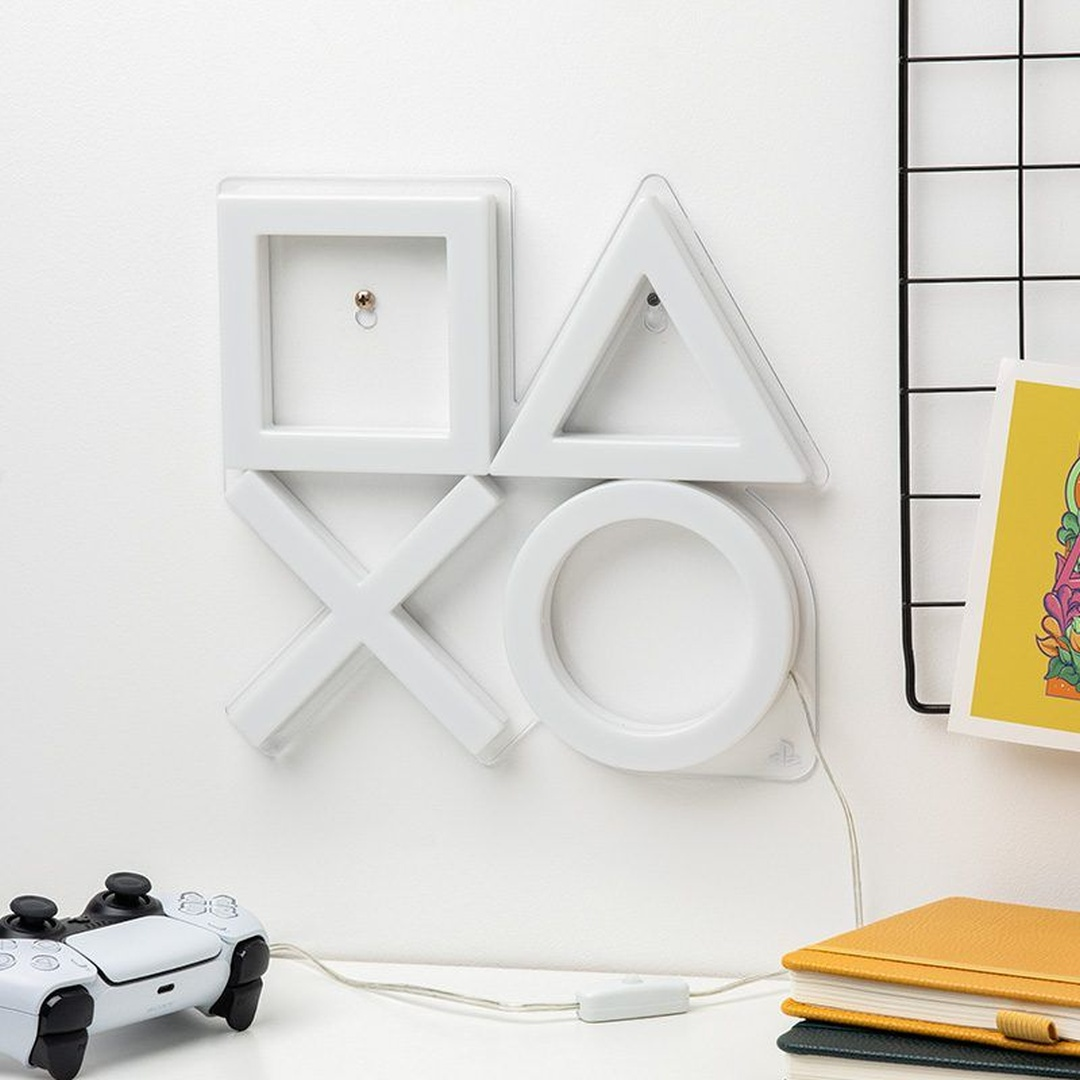 Białe symbole PlayStation jako lampa ścienna z kontrolerem i notatnikami.
