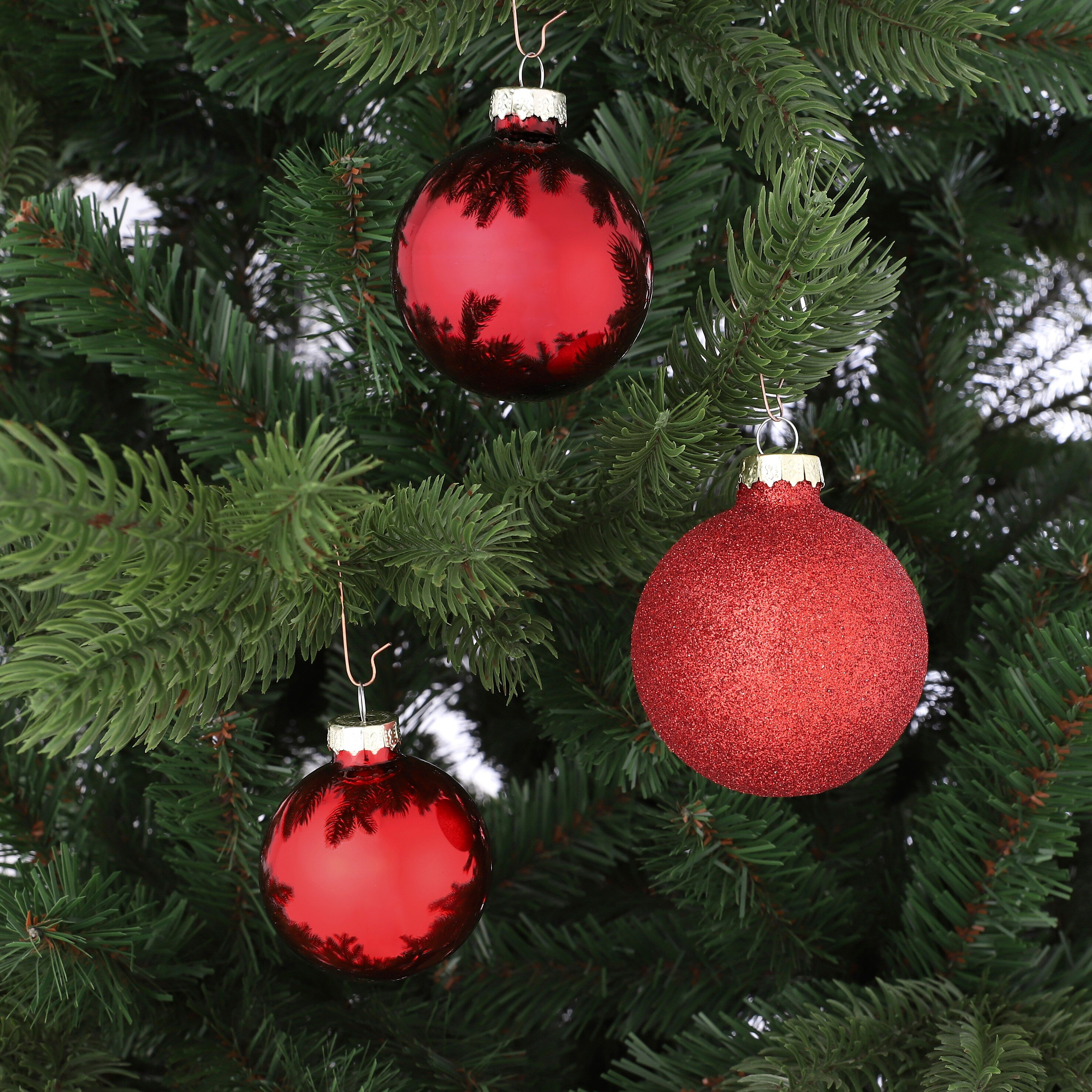 Drie rode kerstornamenten hangen aan een groene boom.