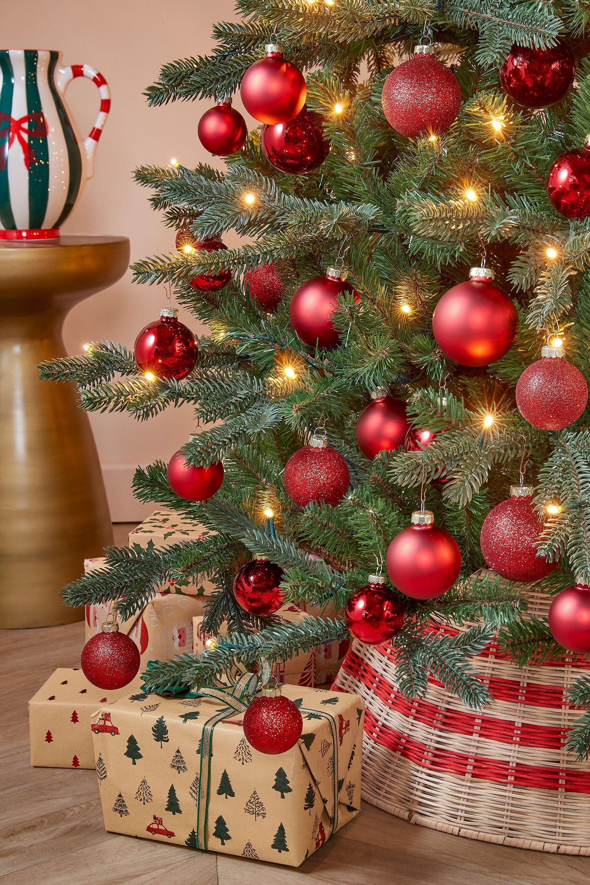Een kerstboom versierd met rode ballen, lampjes en cadeaus aan de voet.