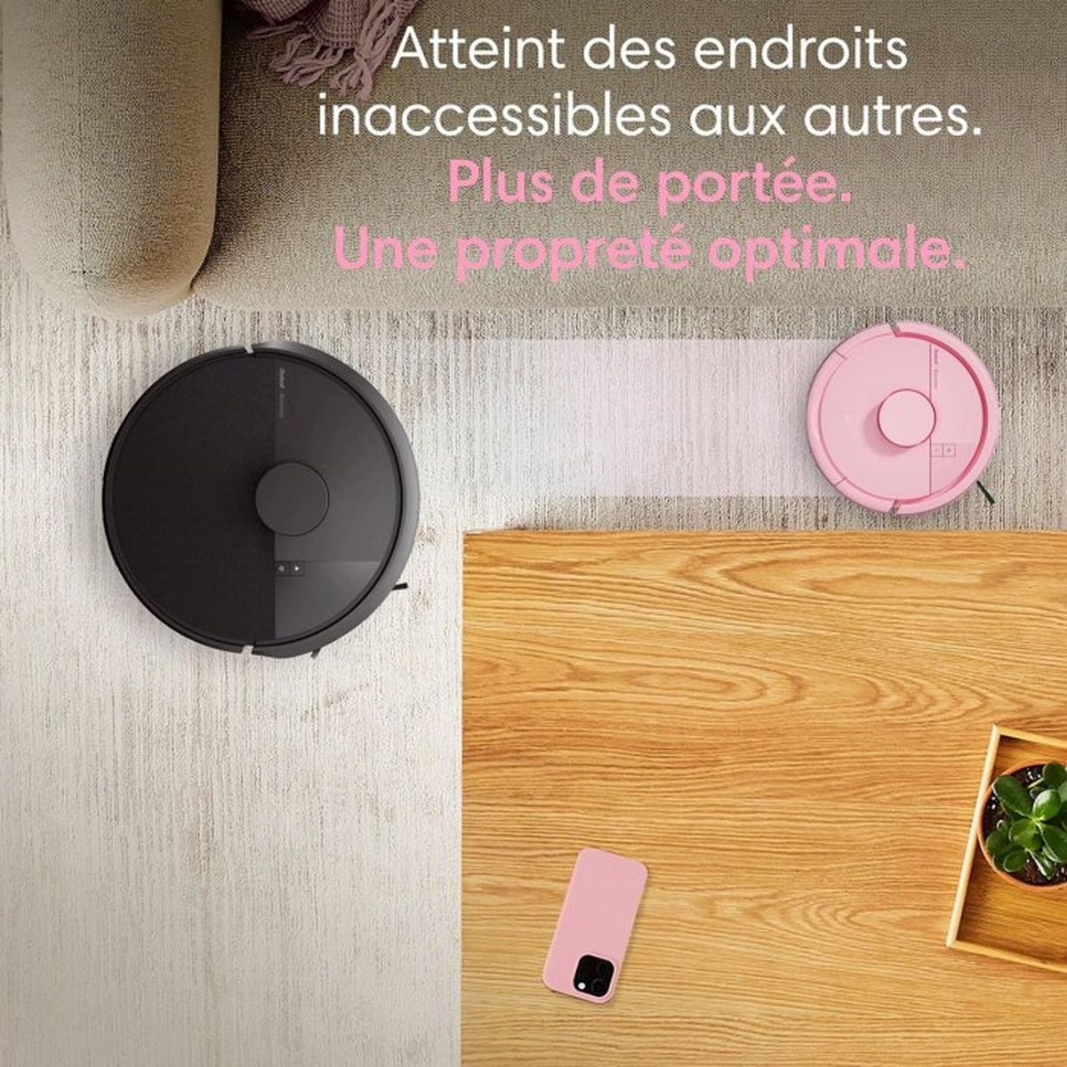 Un robot aspirapolvere nero e uno rosa su tappeto e pavimento in legno.