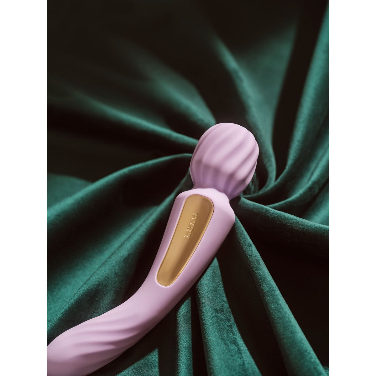 Un vibrador morado acanalado descansa sobre una tela verde oscuro brillante.